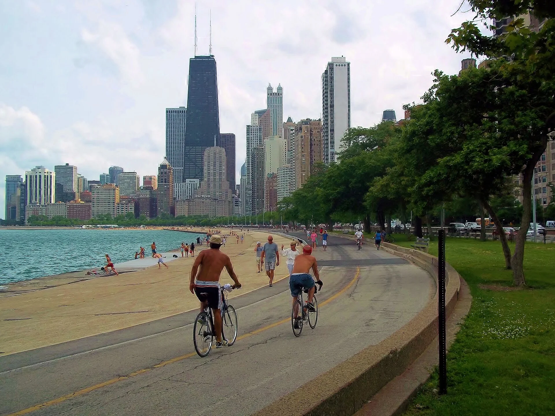 Chicago lakefront view with Willis Tower skyline, sandy beach, cyclists and swimmers enjoying waterfront recreation
