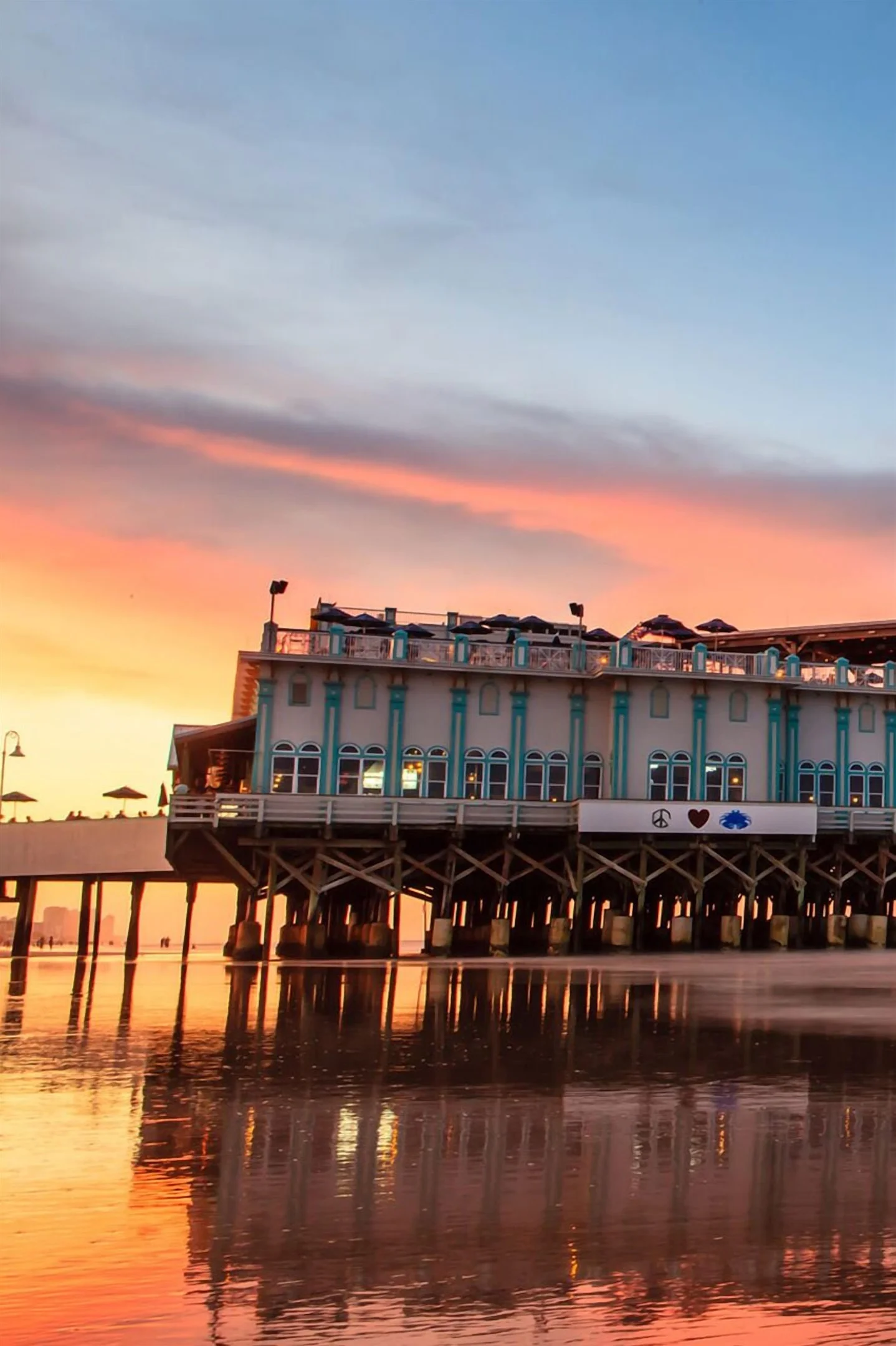 Beachfront boardwalk building at sunset with turquoise windows and ocean view pricing calendar overlay in Daytona Beach