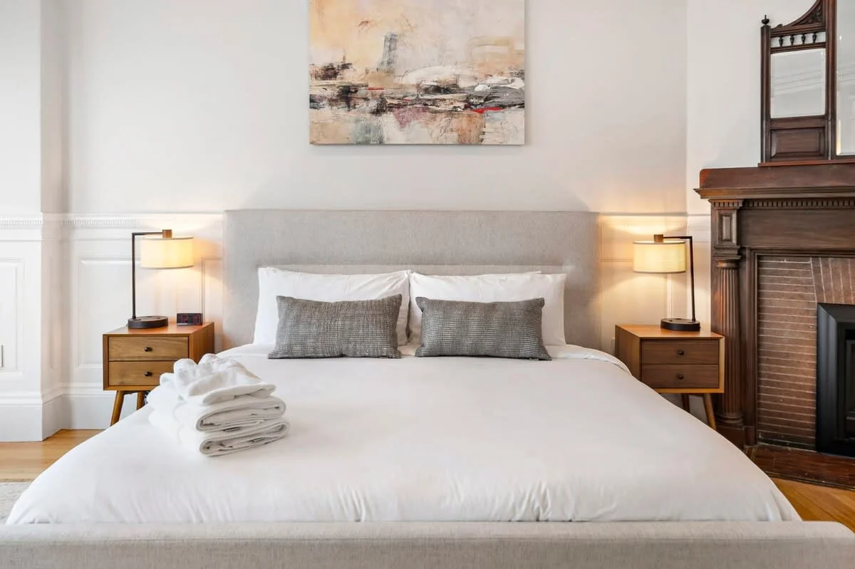 Housekeeper folding white linens on queen bed in turnover cleaning service for Boston Airbnb rental management