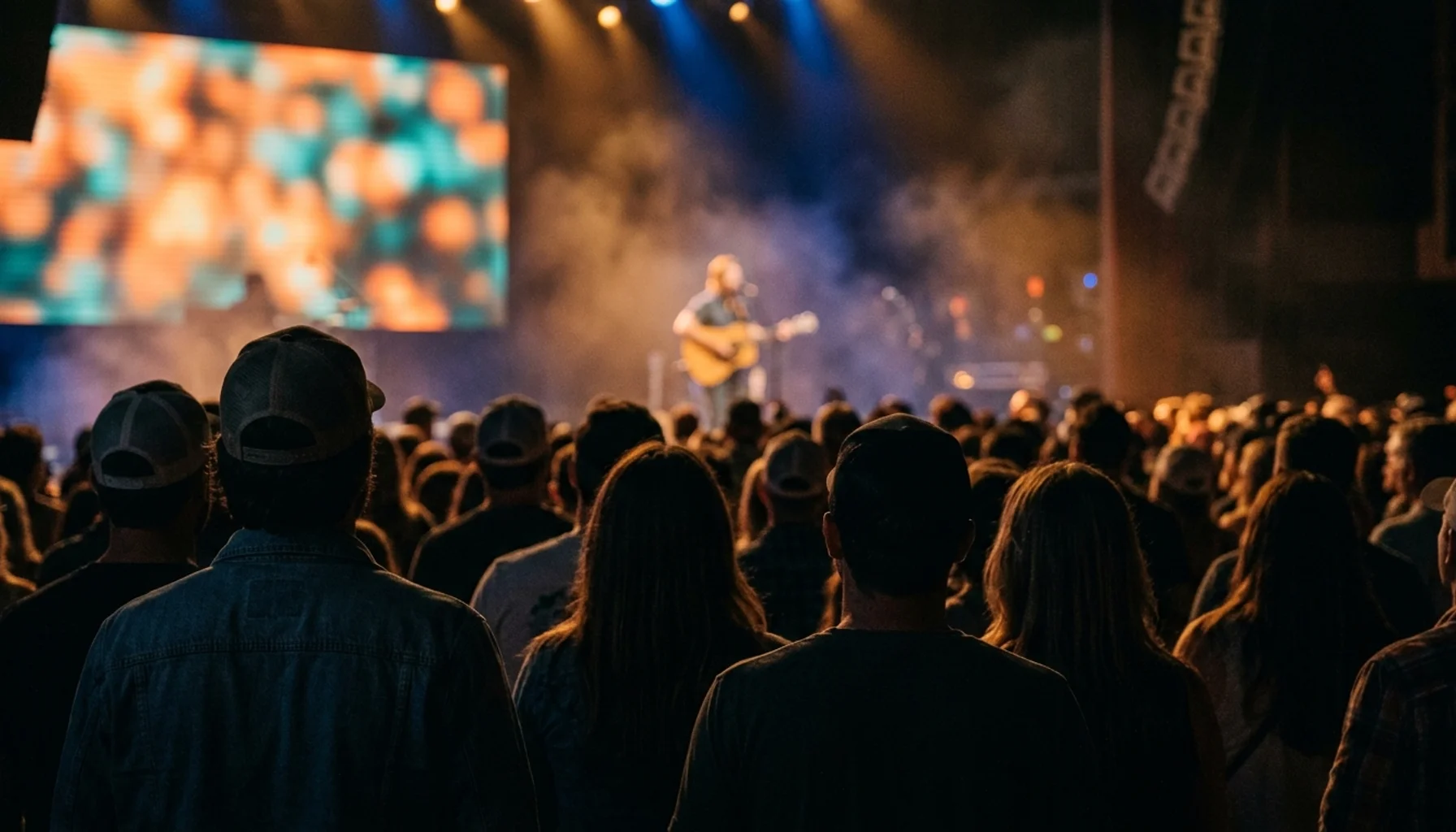 Crowd silhouettes at an Americana music festival and conference showcase in a Nashville venue, stage lights cutting through haze