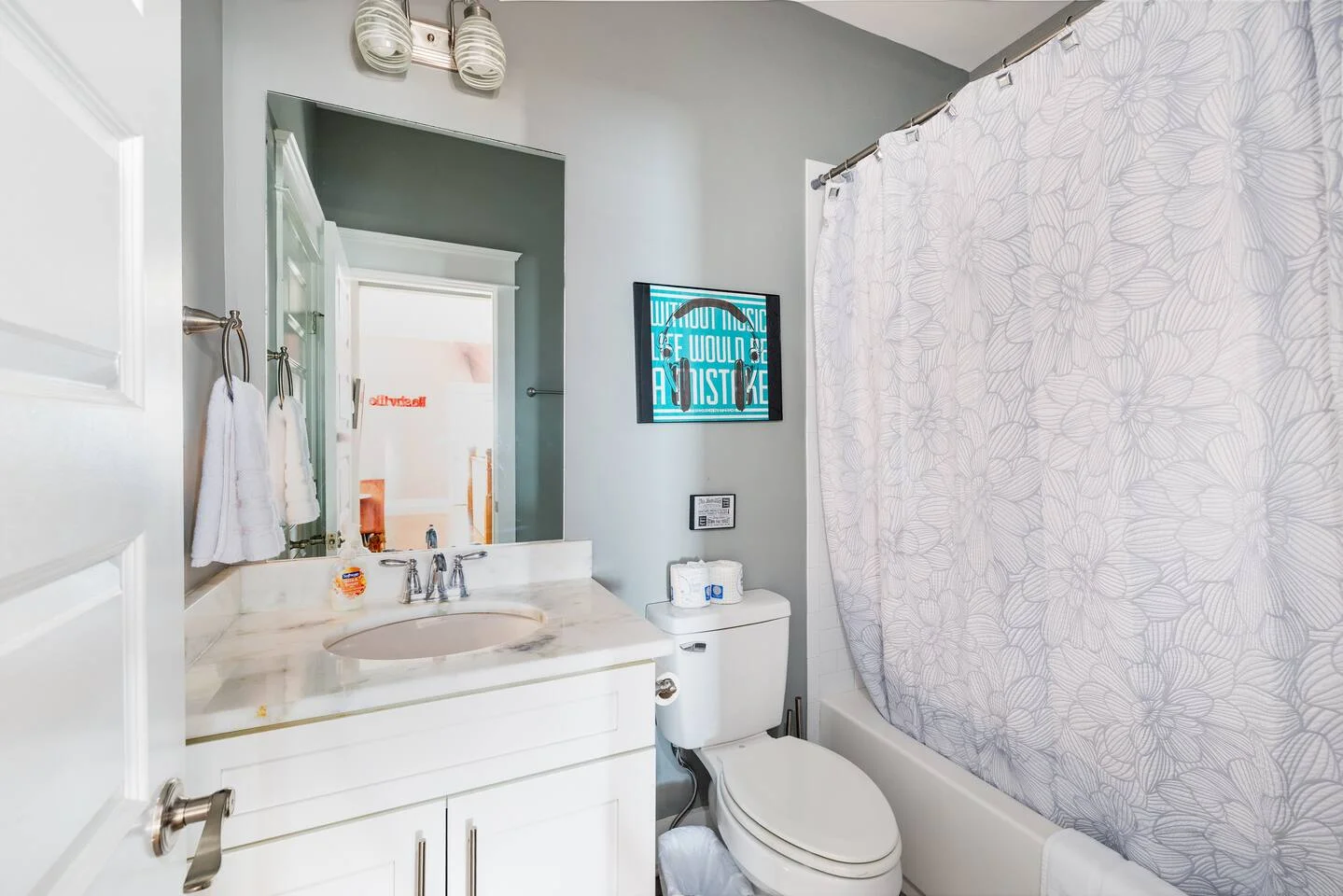 Modern bathroom with marble vanity, sage green accent wall, and neon sign in Nashville vacation rental