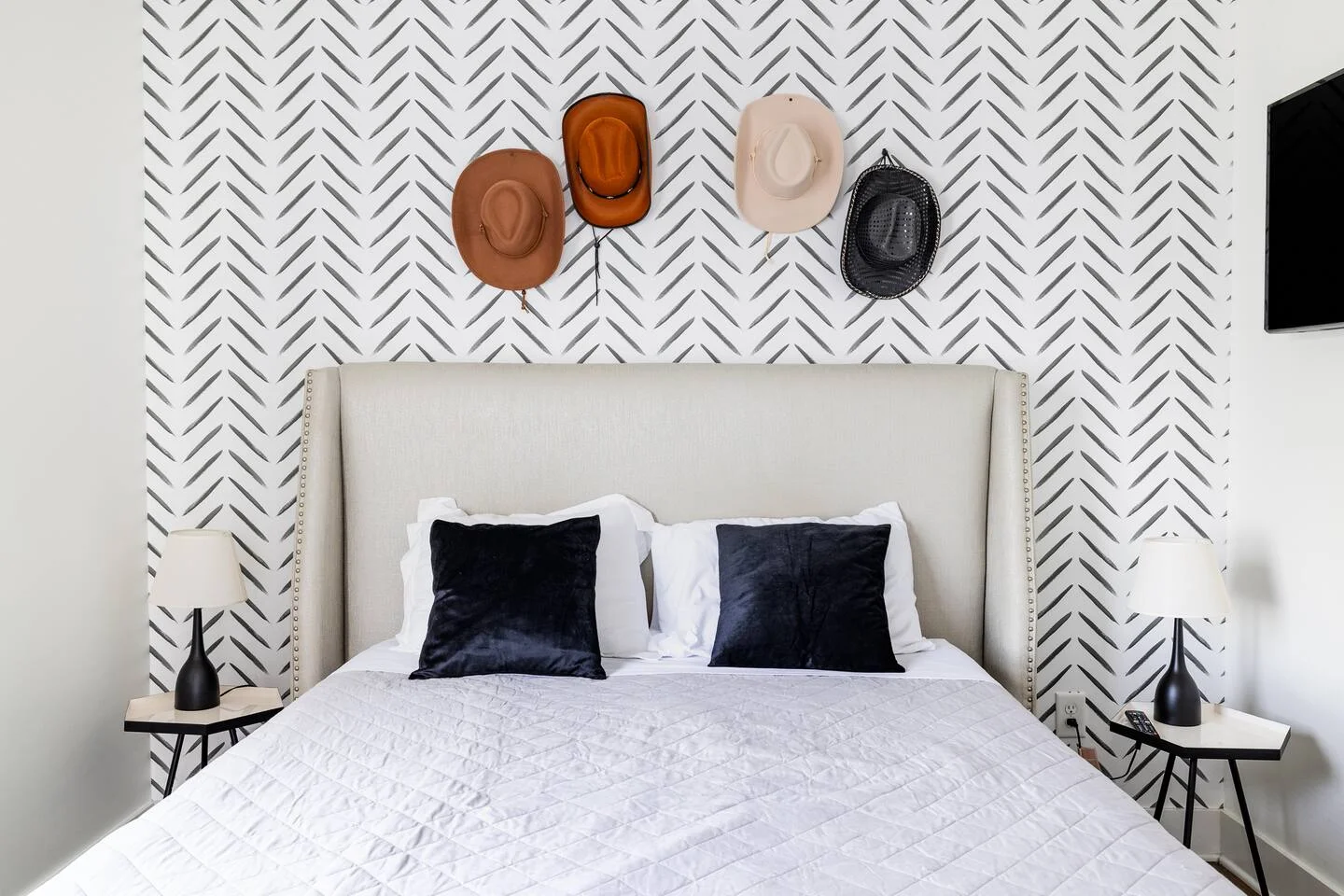 Modern bedroom with herringbone accent wall, upholstered headboard, and cowboy hats display in Nashville luxury vacation