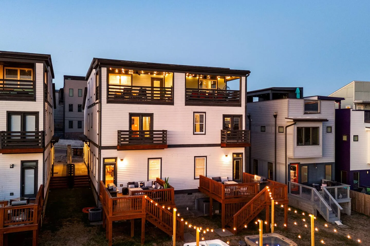 Modern three-story white home with illuminated decks and string lights, Nashville TN vacation rental hot tub backyard