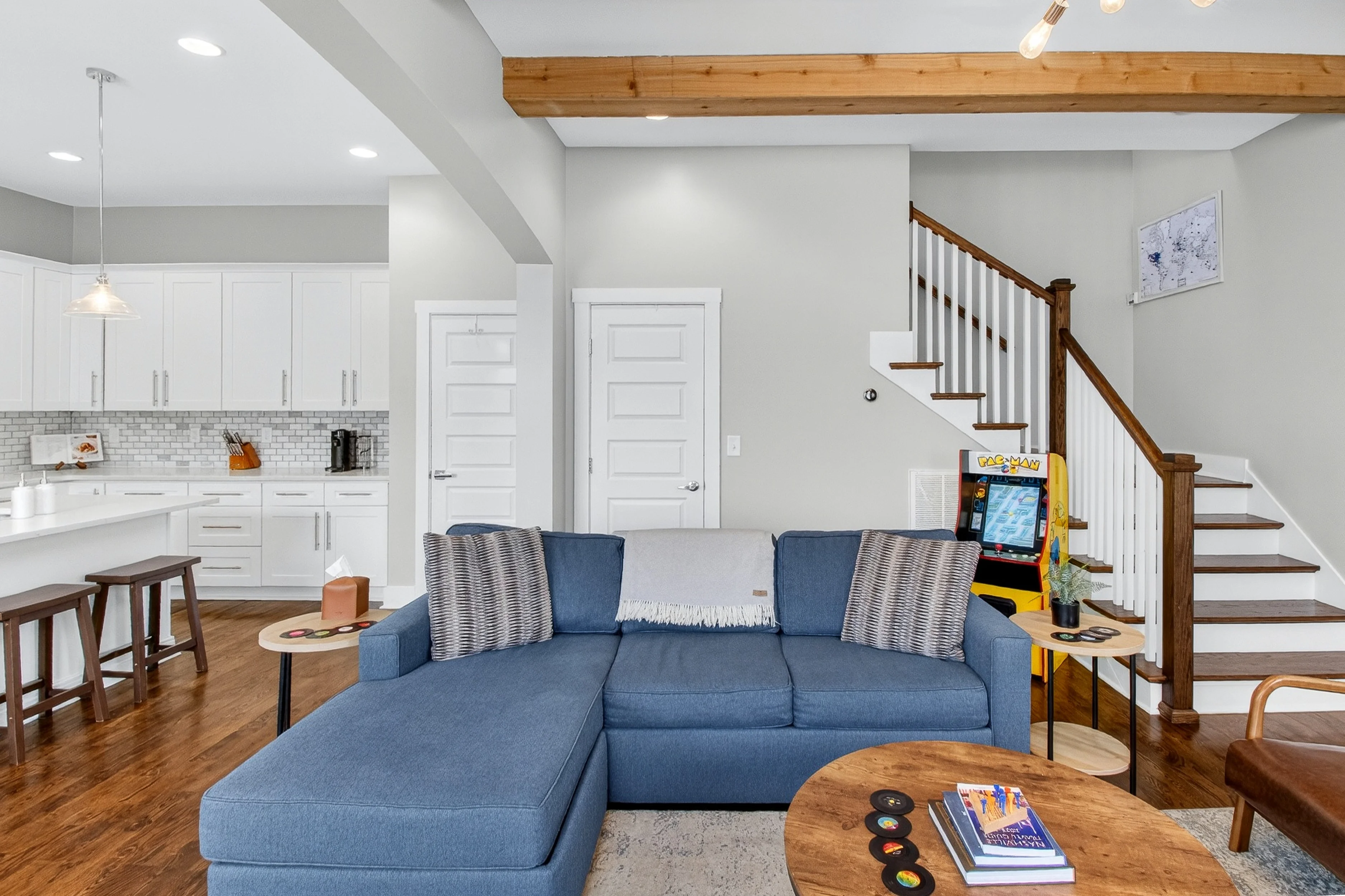 Modern open-concept living room with blue sectional sofa, white kitchen cabinetry, and wooden staircase at Nashville