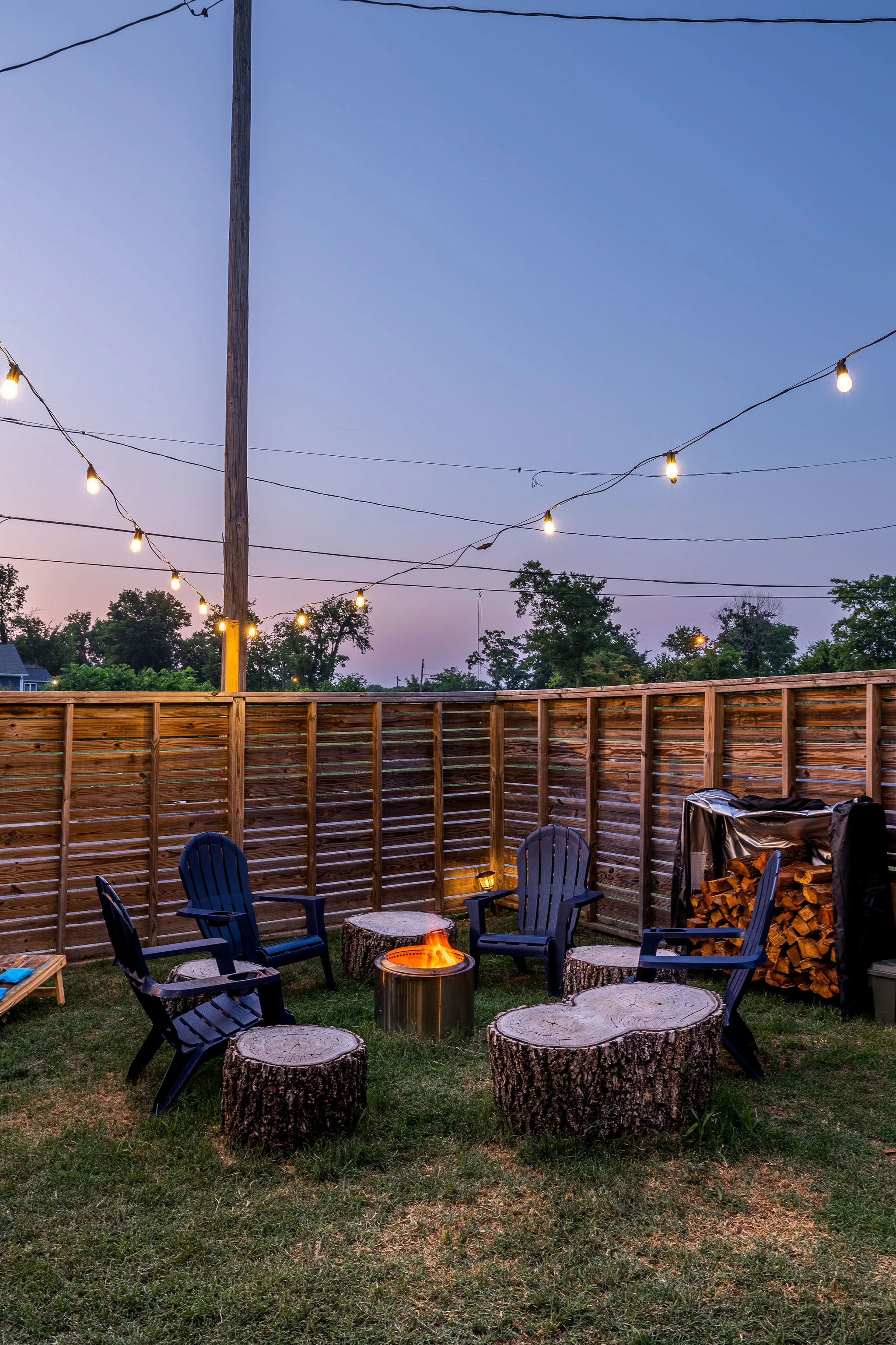 Outdoor patio with fire pit, Adirondack chairs, and string lights at dusk at Underwood Manor Nashville
