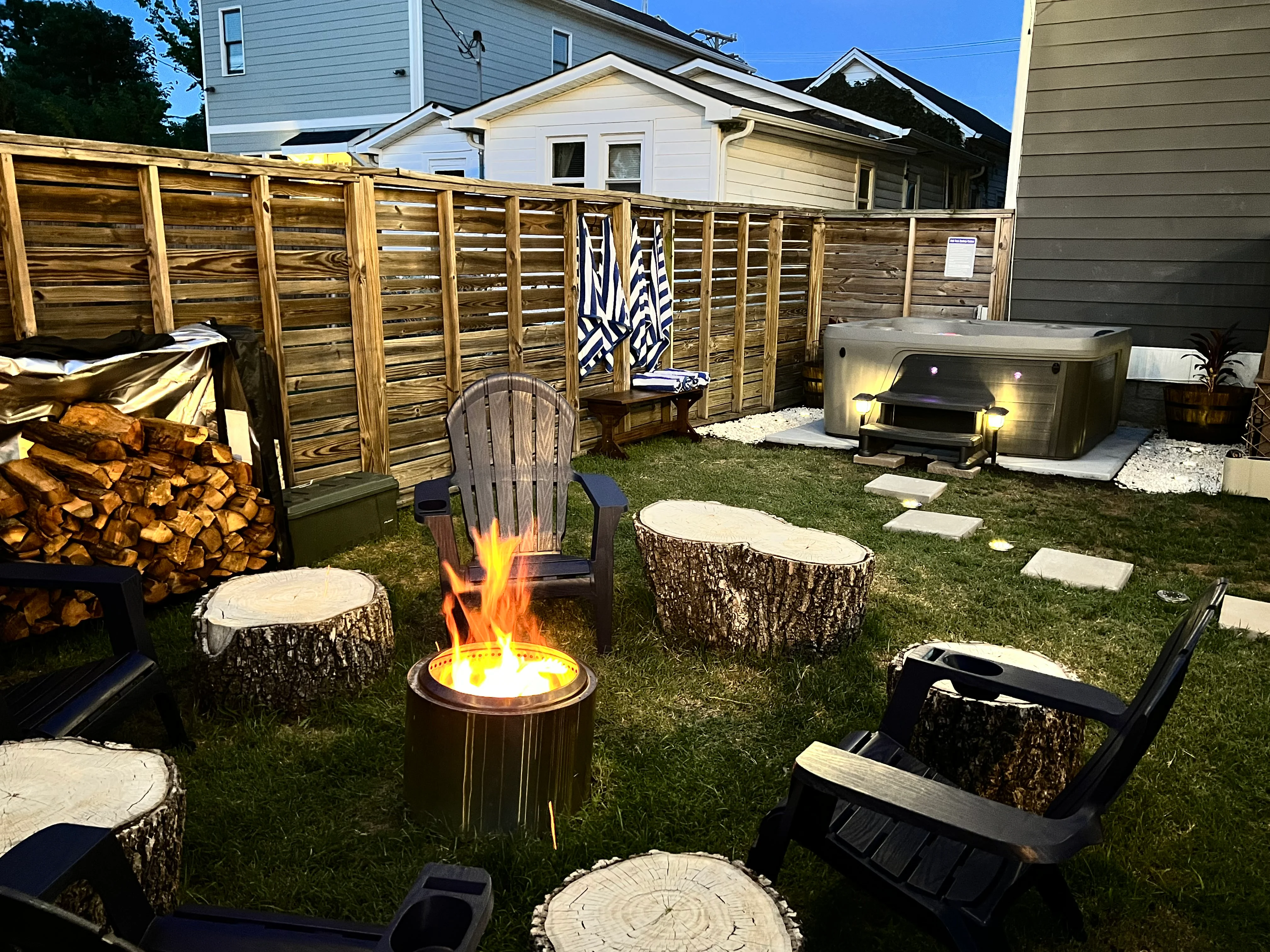 Backyard fire pit with rustic log seating and hot tub at Underwood Manor Nashville outdoor entertainment space