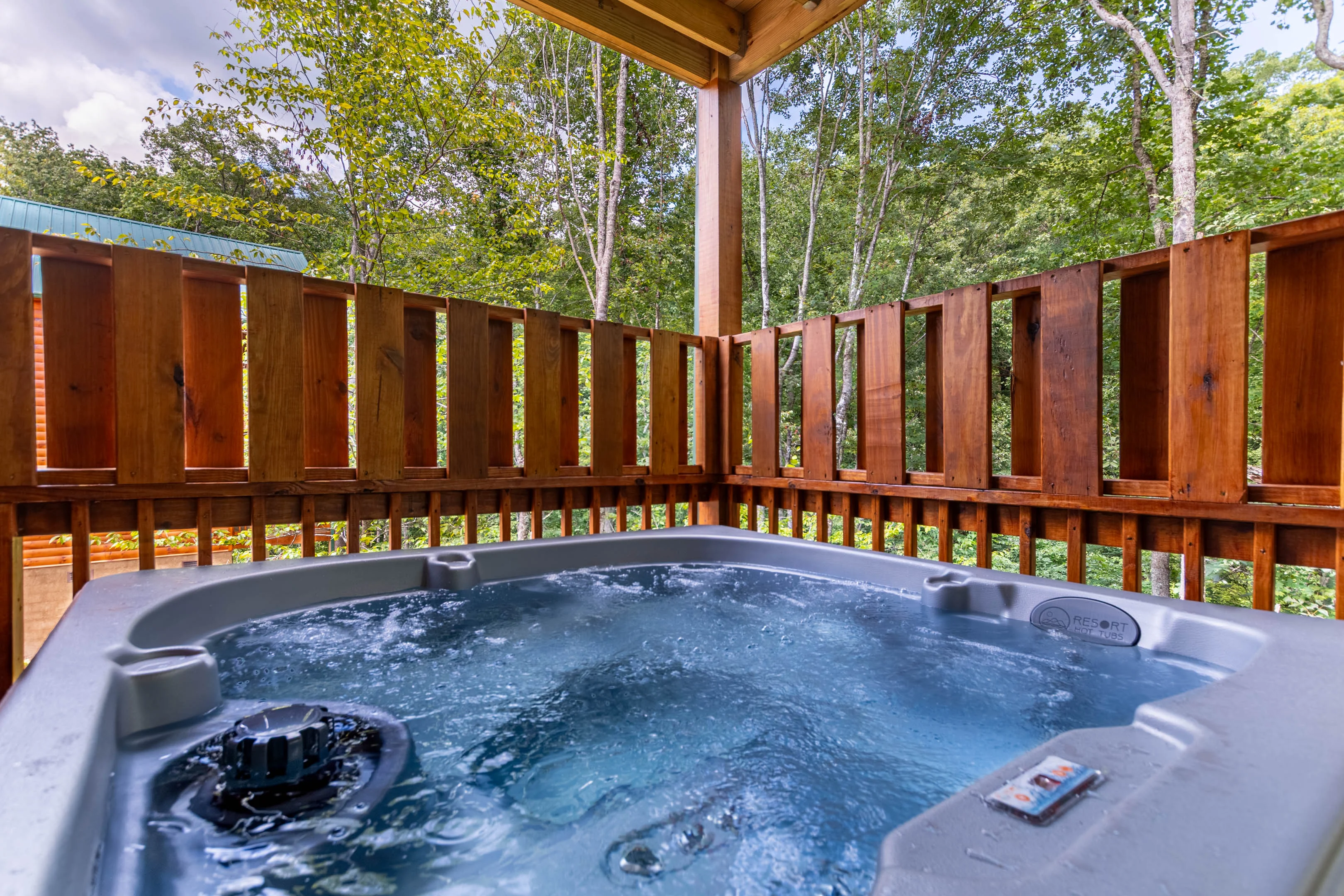 Hot tub on wooden deck at luxury Gatlinburg TN cabin with pool, surrounded by forested mountain views