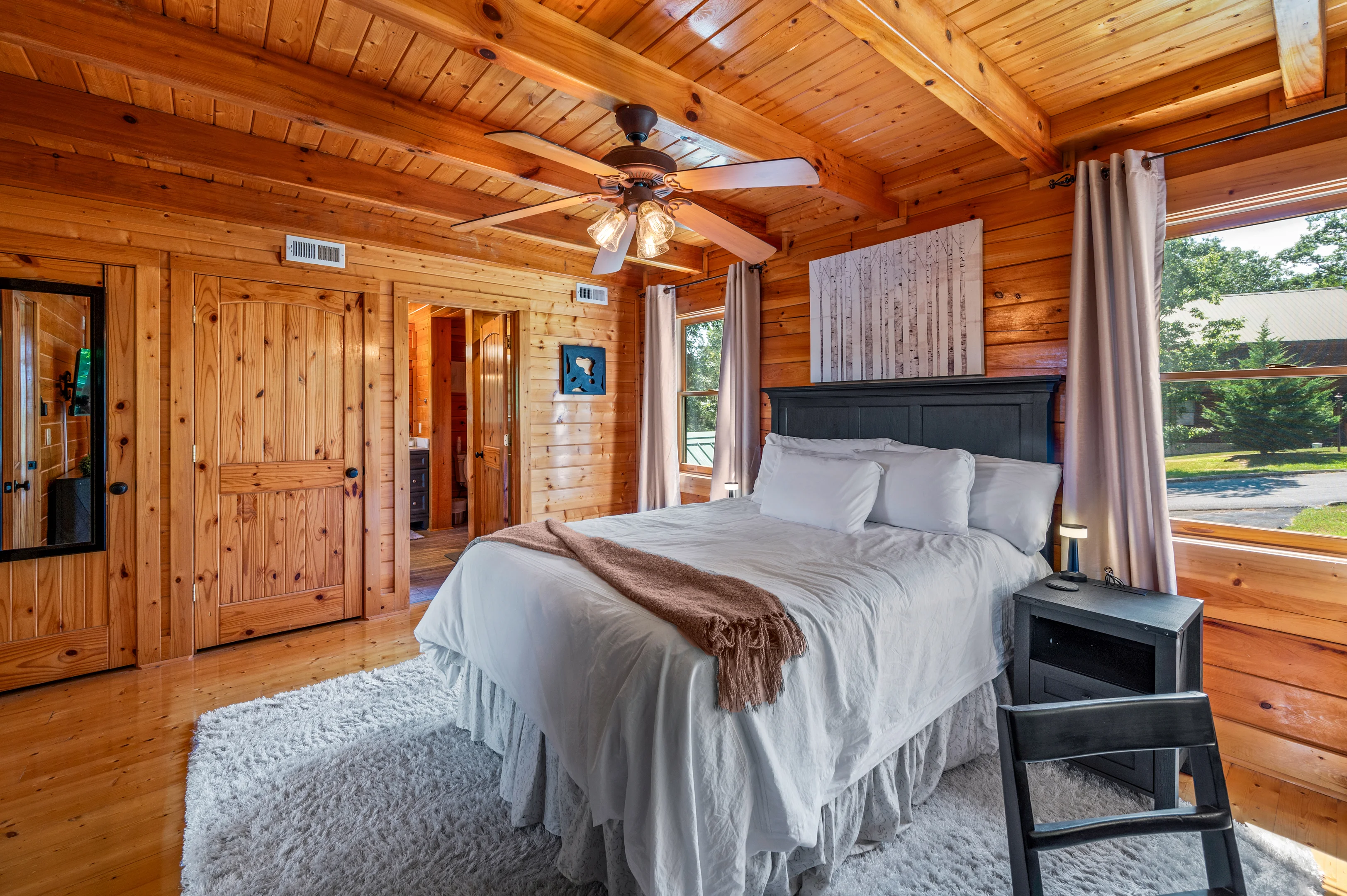 Master bedroom in a rustic log cabin with king bed, wooden beams, and forest views near Sevierville TN