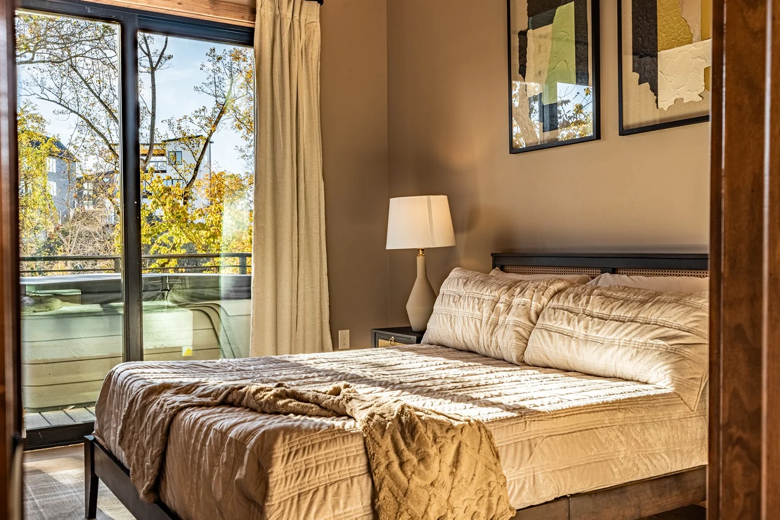 Master bedroom with queen bed, neutral bedding, and glass doors opening to tree-lined balcony at Smoky Mountain Serenity