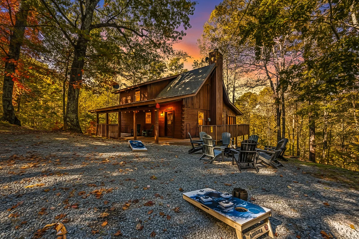 Rustic cabin in forest with Adirondack chairs and cornhole during golden sunset, showcasing Pigeon Forge TN vacation rental