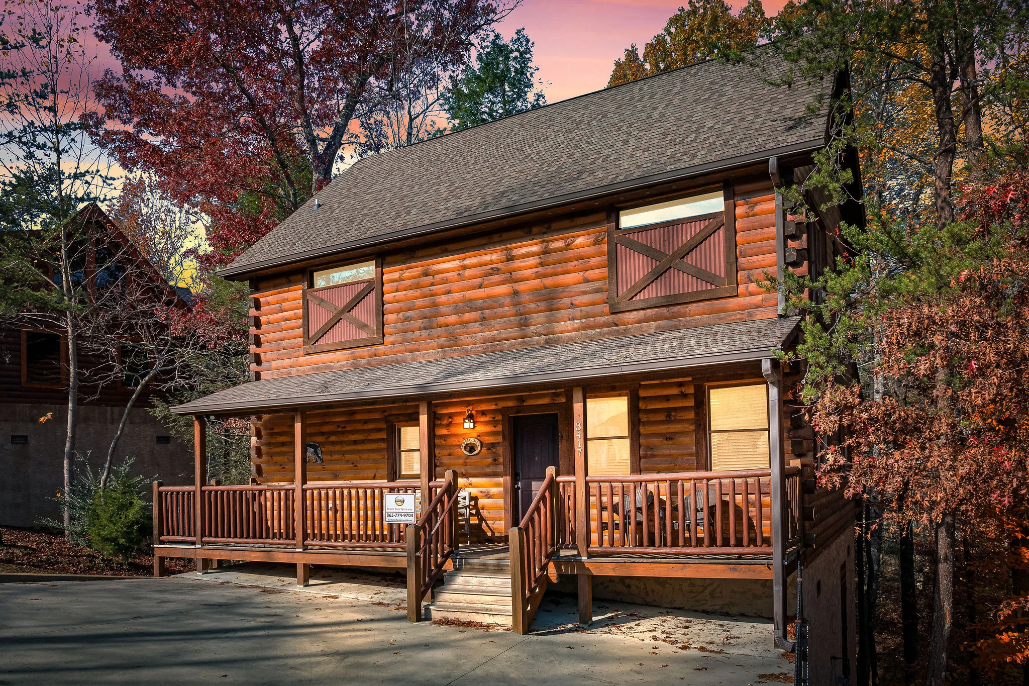 Log cabin exterior at dusk with illuminated decks and autumn foliage, romantic couple getaway Sevierville TN