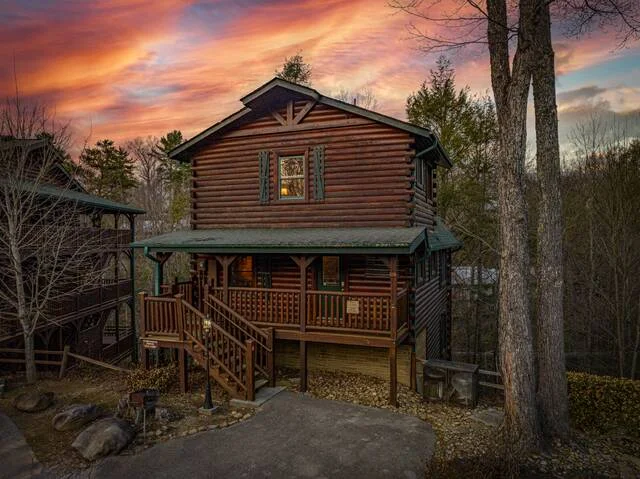 Rustic log cabin exterior in Sevierville with wraparound porch nestled in trees, perfect for romantic getaways in Gatlinburg Sevierville TN