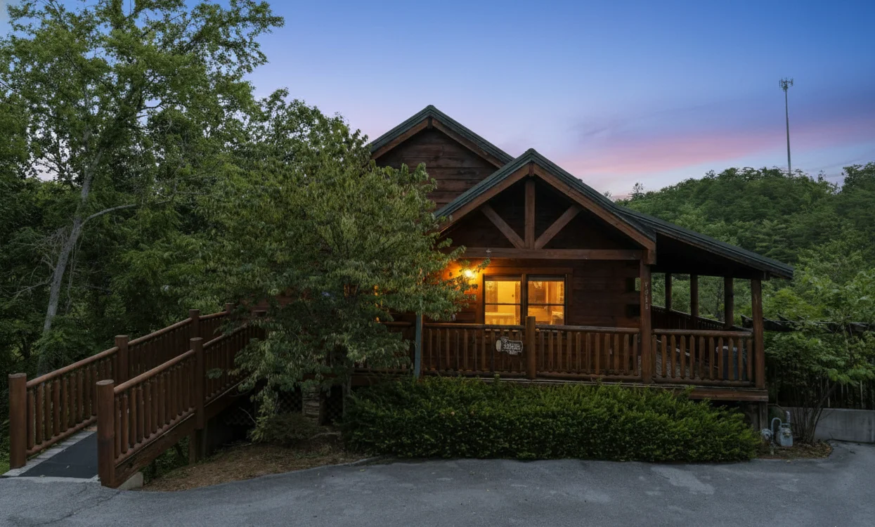 Rustic wood cabin with lit porch at dusk surrounded by trees