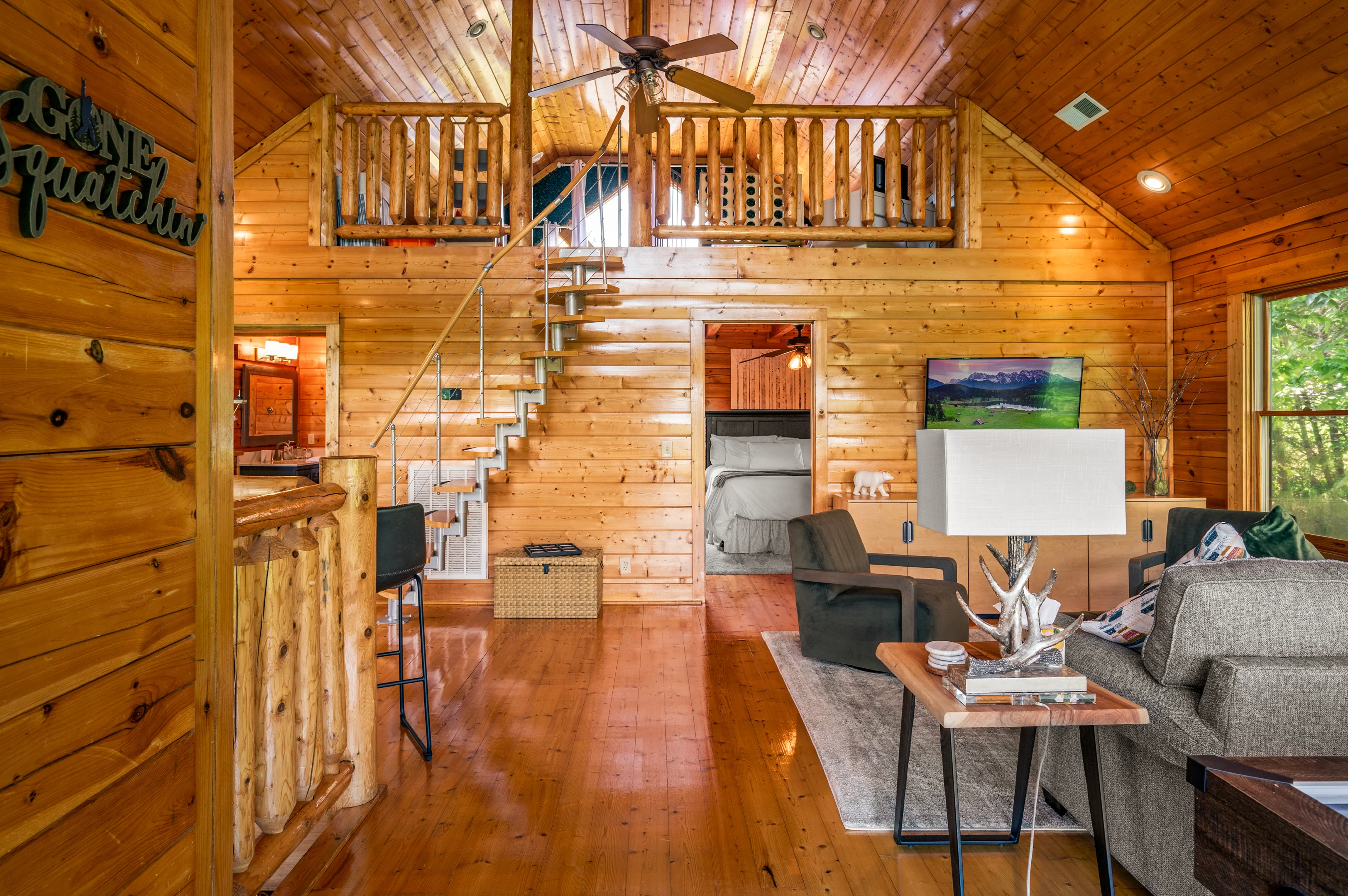 Open-concept log cabin living room with loft bedroom and mountain view, exemplifying property management revenue