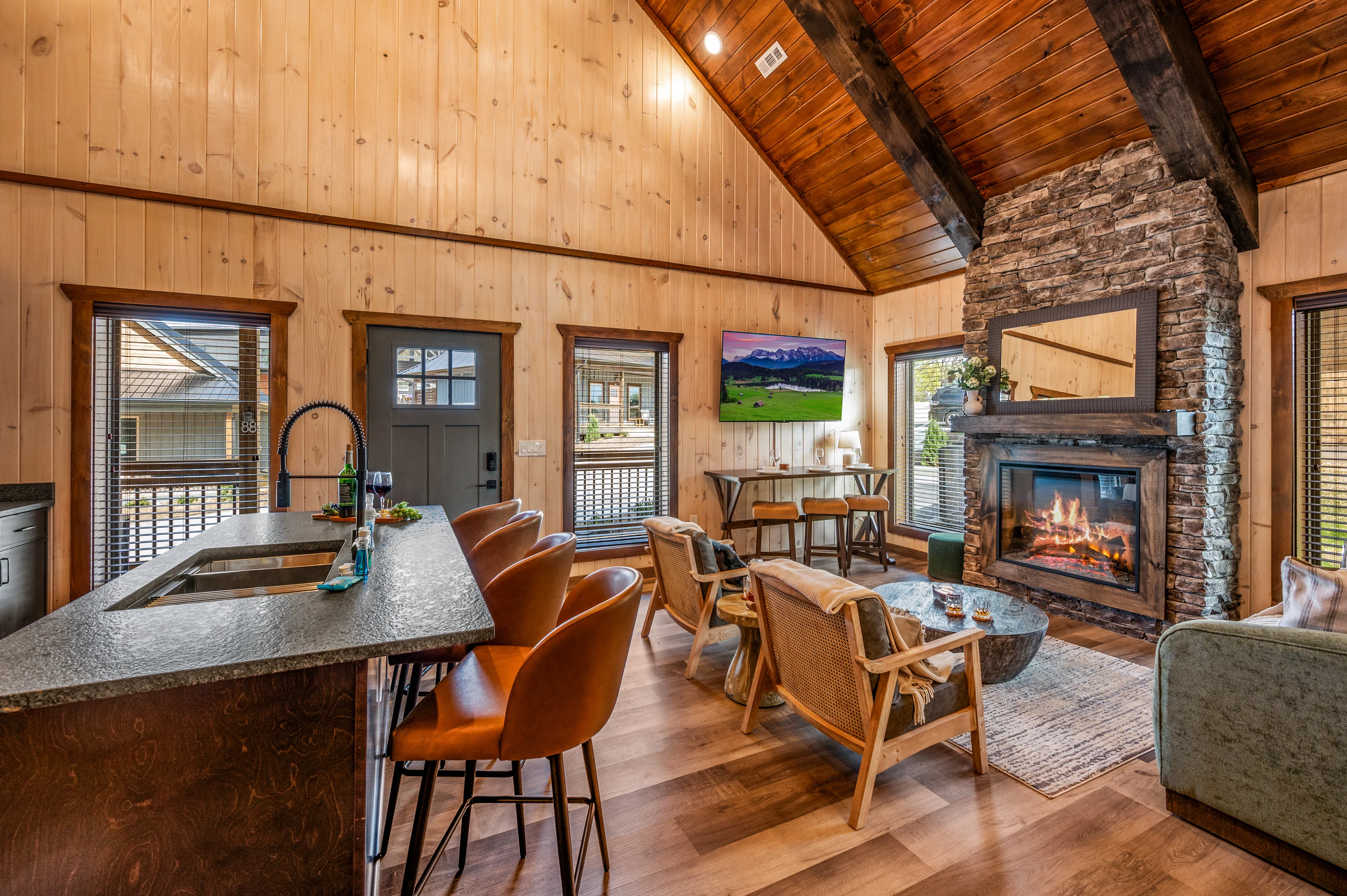 Luxury cabin living room with wood paneling, stone fireplace, and mountain views through large windows