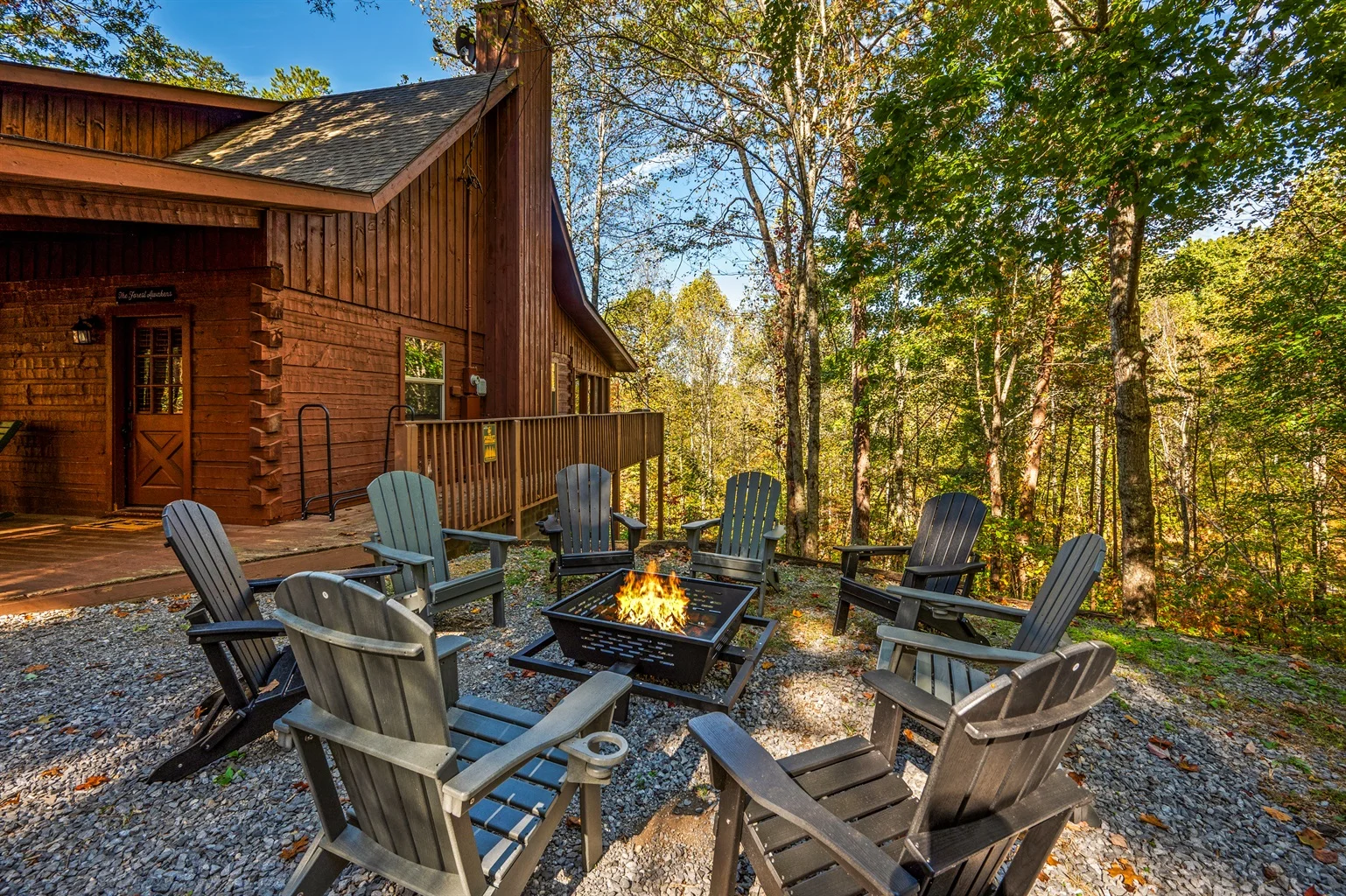 Rustic log cabin patio with fire pit and Adirondack chairs surrounded by forest trees at The Forest Awakens luxury vacation