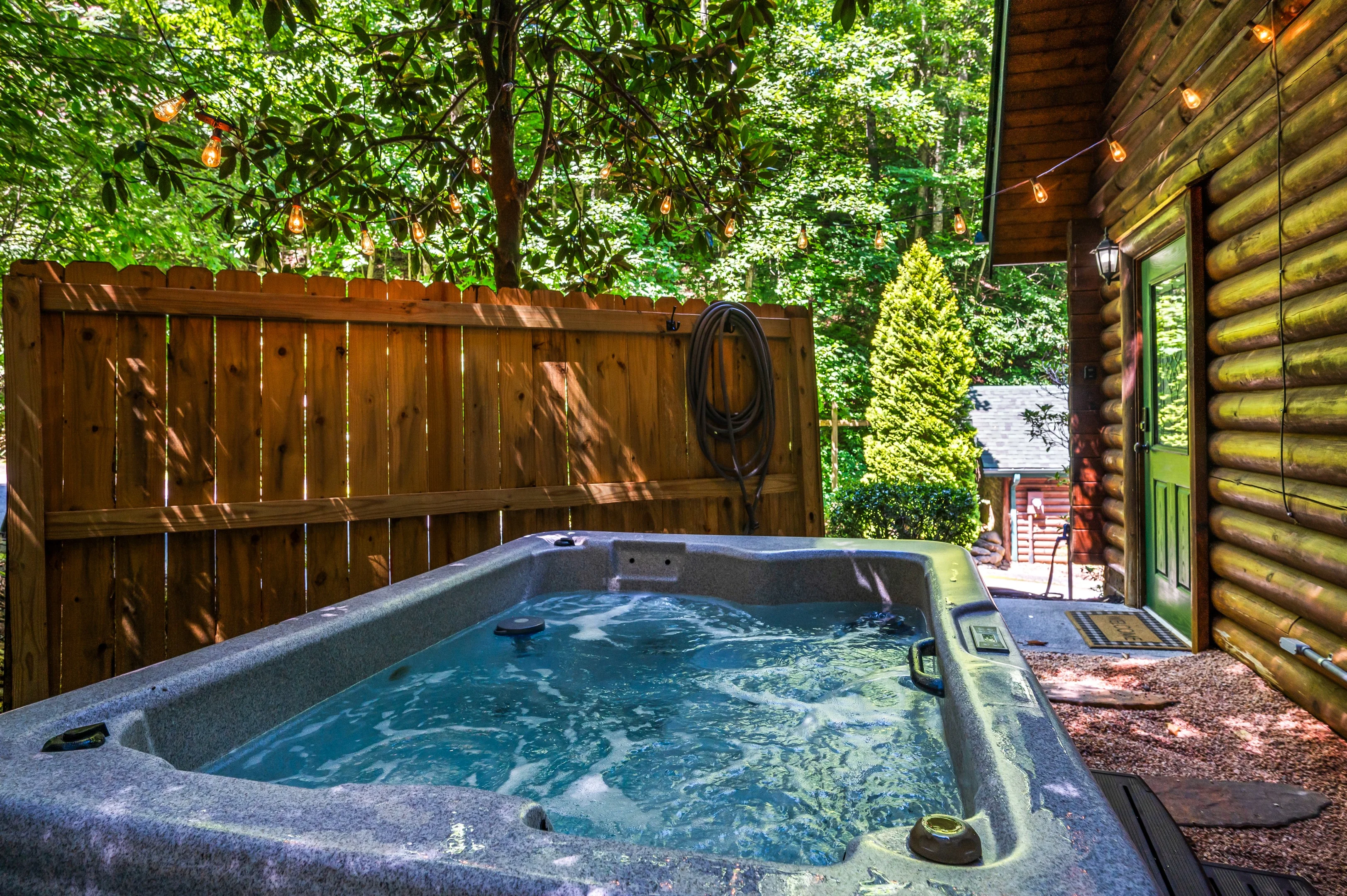 Private hot tub on wooded patio at affordable Gatlinburg cabin rental with string lights and log cabin setting