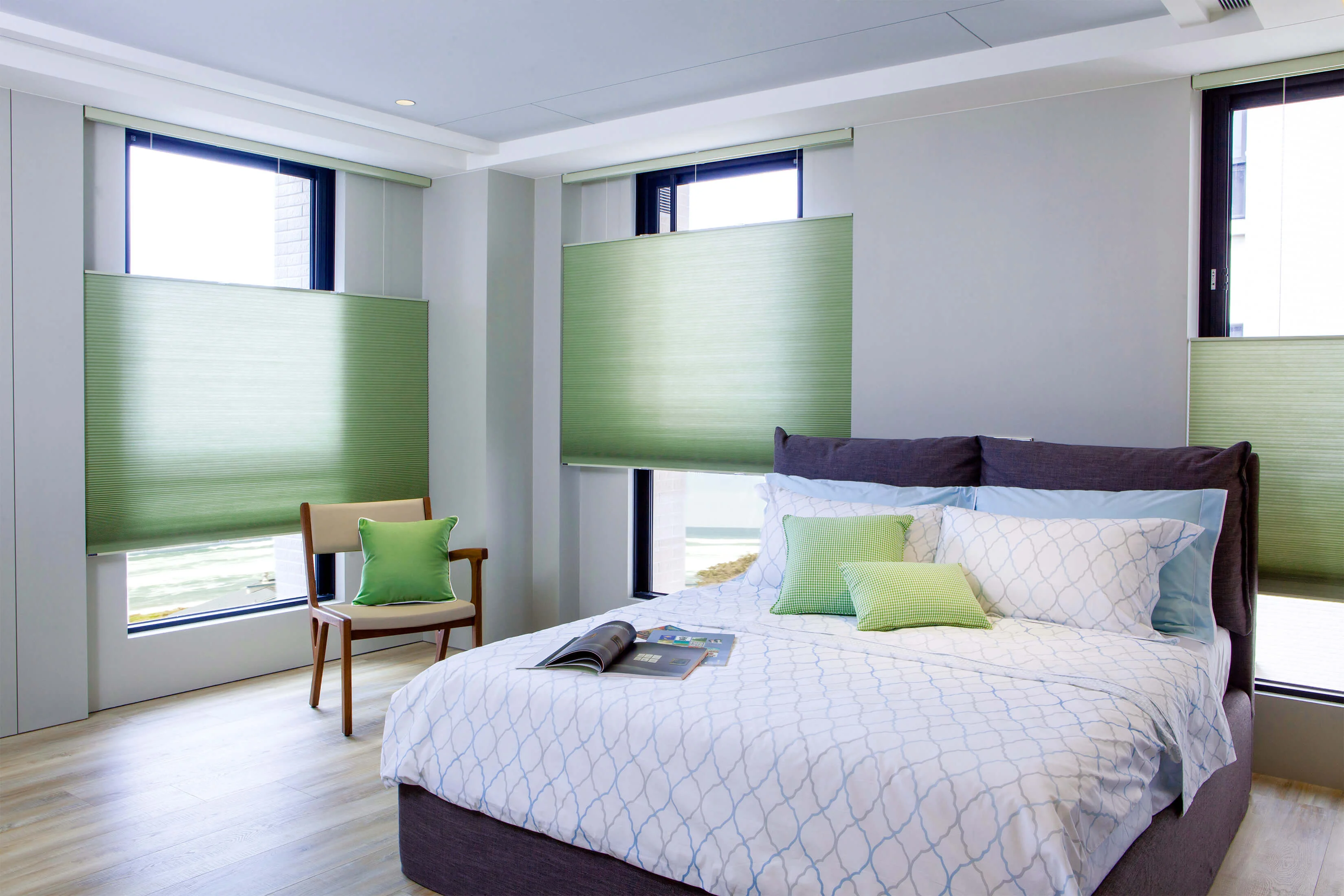 Modern bedroom with king bed, green blinds, accent chair, and abundant natural light