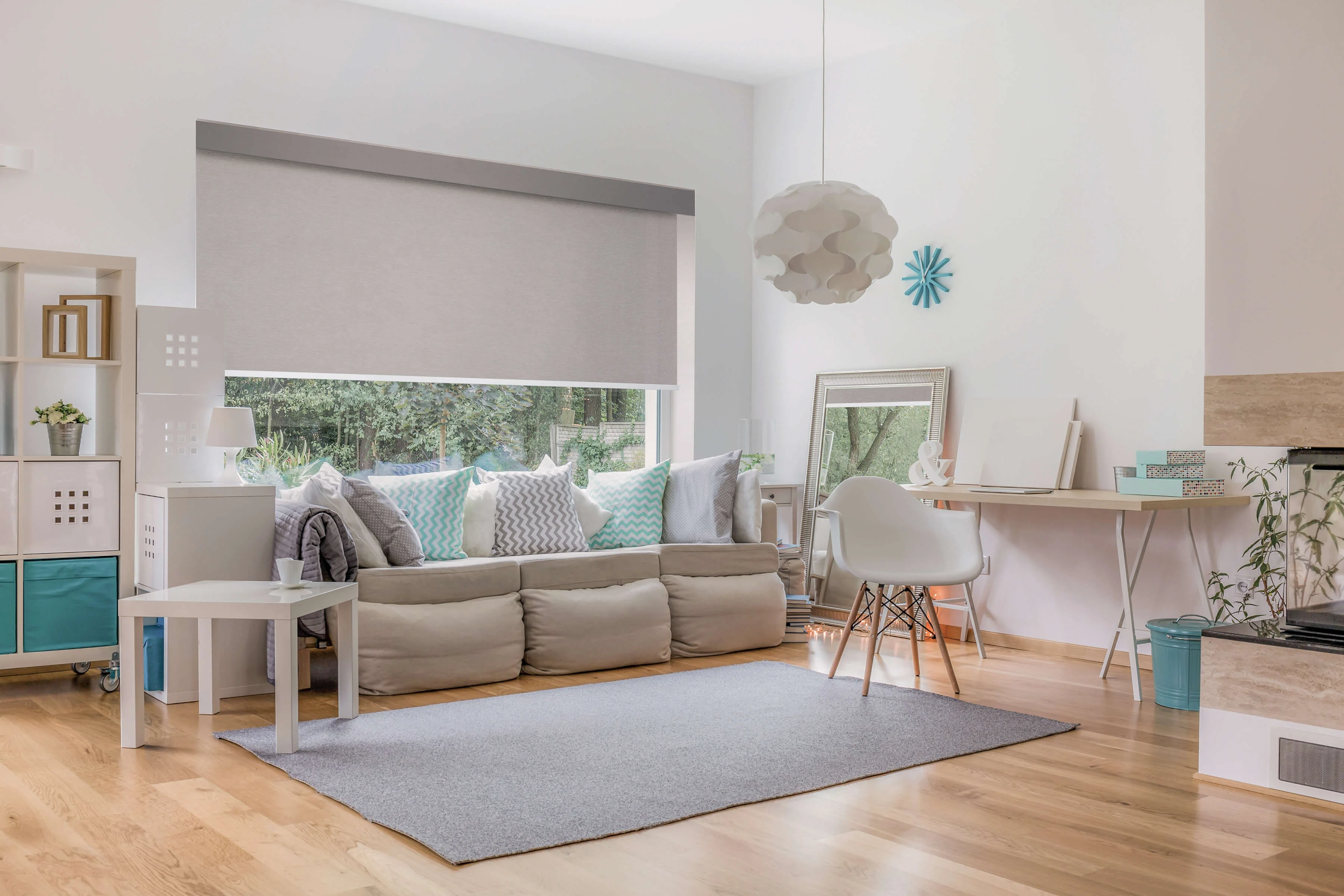 Modern living room with beige sectional sofa, turquoise accents, forest views, and integrated home office desk