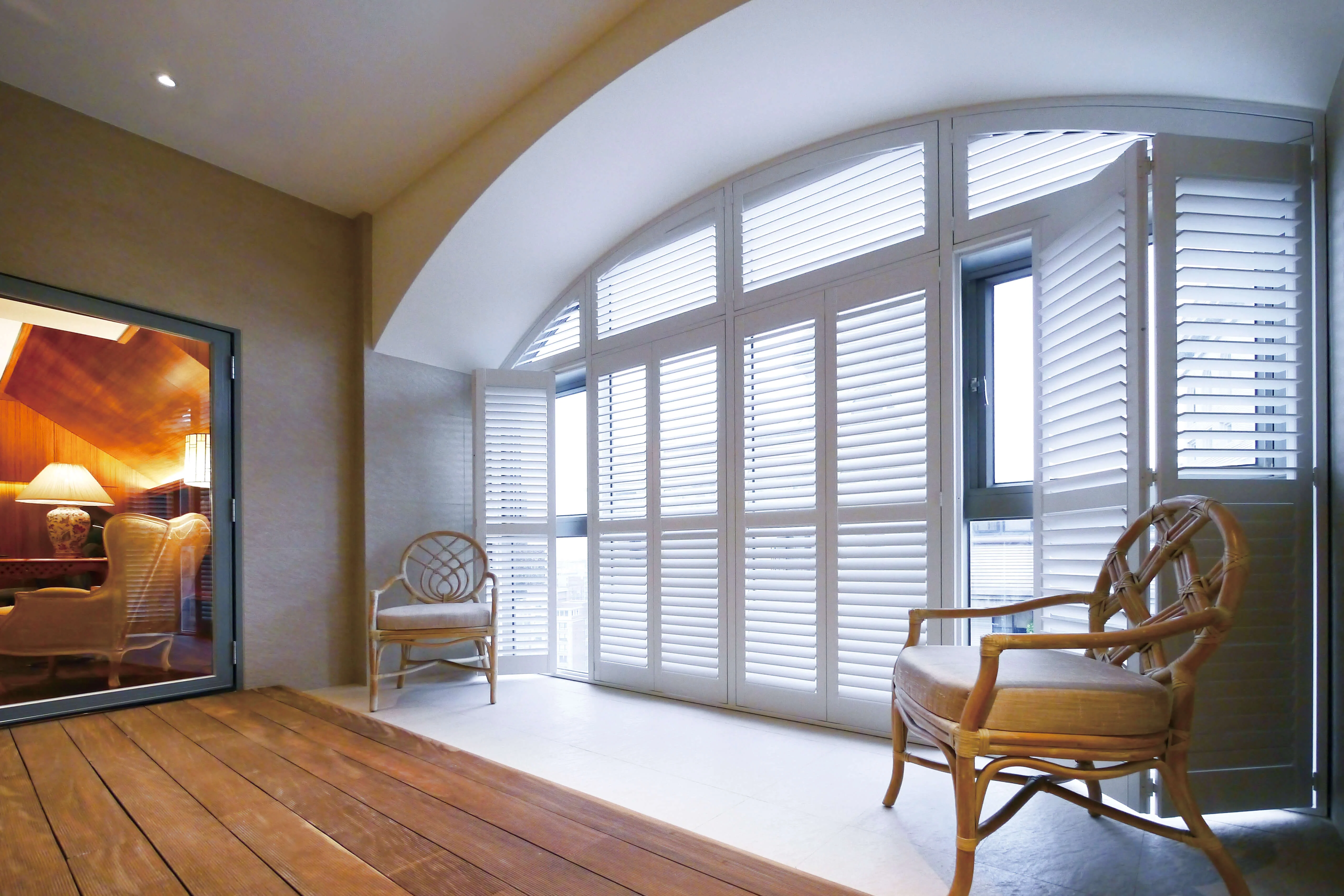 Bright sunroom with arched windows, white plantation shutters, and rattan chairs