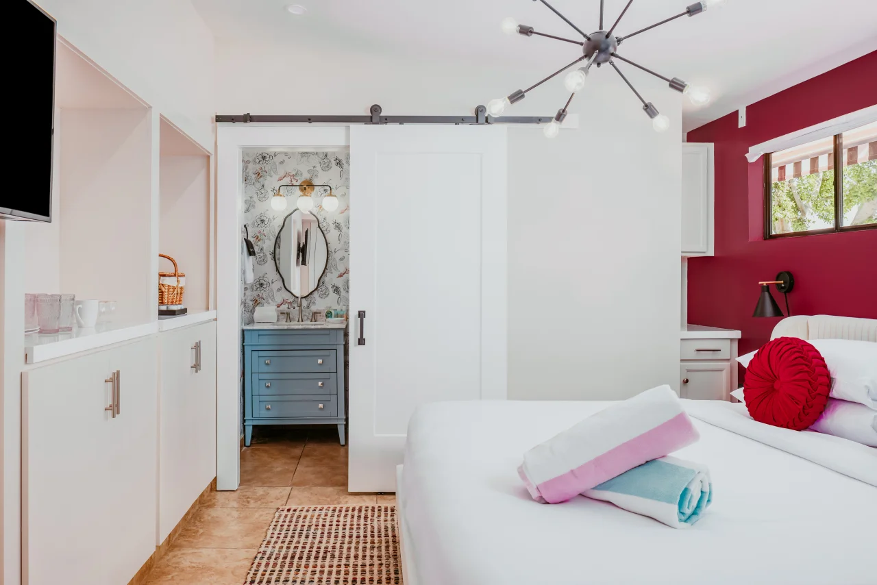 Boutique hotel Palm Springs suite with queen bed, red accent wall, blue vanity bathroom, and mid-century luxury design