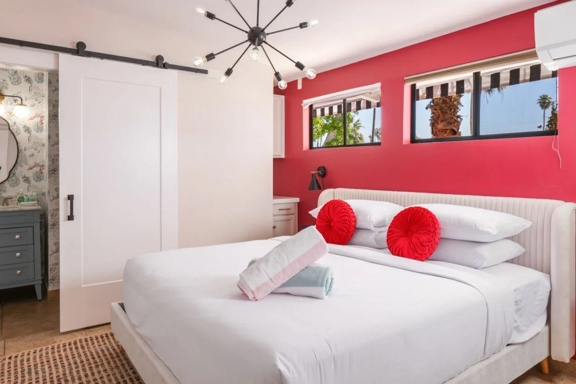 The Edie Suite bedroom with coral pink accent wall, white upholstered bed, and contemporary black lighting showcasing