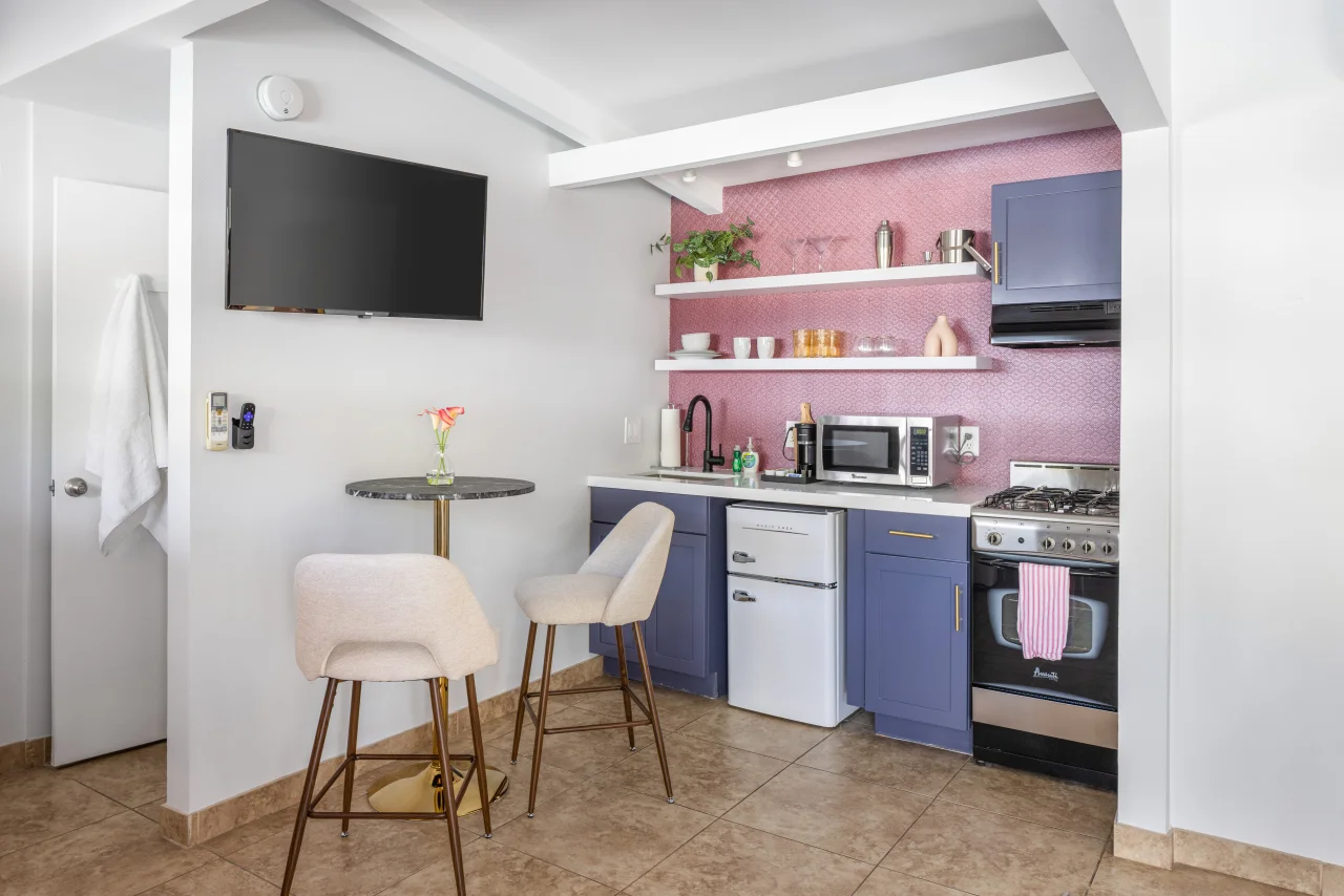Modern kitchenette with pink textured accent wall, navy cabinetry, and stainless steel appliances at The Sofia Suite in Palm