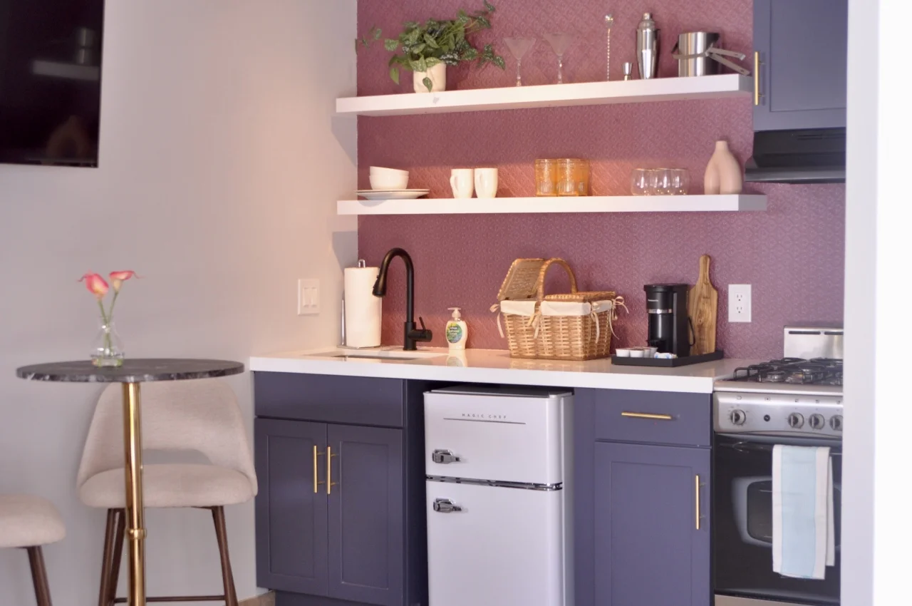 Modern kitchenette with purple cabinets, white shelves, and vintage refrigerator in a mauve-walled suite