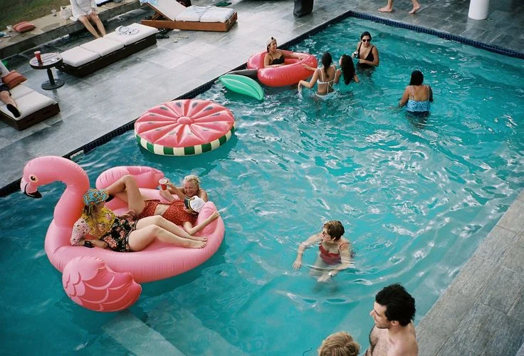 Guests enjoying vibrant inflatable pool floats in a turquoise swimming pool with white lounge chairs