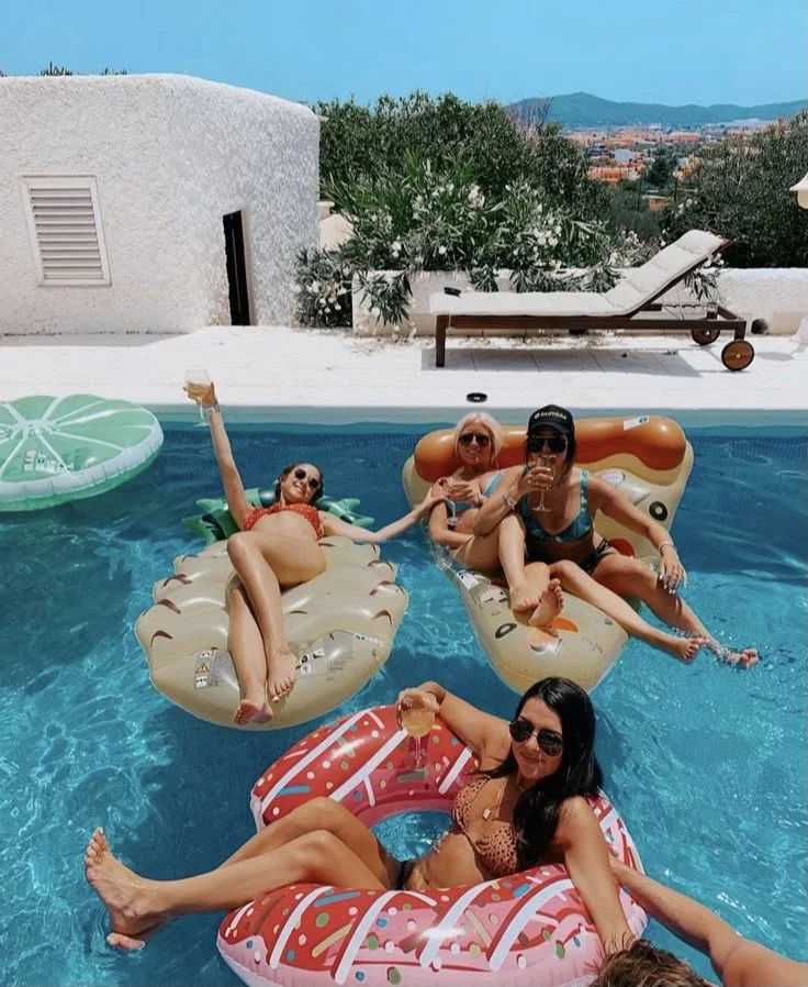 Guests on colorful pool floats in resort pool with white architecture and mountain backdrop