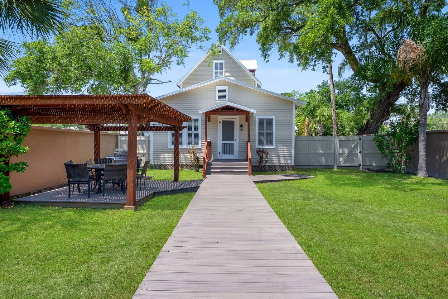 White cottage exterior with mature oak and palm trees, manicured lawn, and pergola representing quality property management