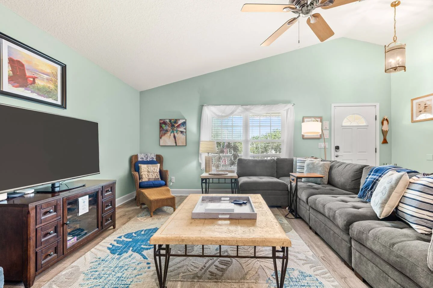Coastal vacation rental living room with mint-green walls, sectional sofa, and warm natural light reflecting 2026 design trends