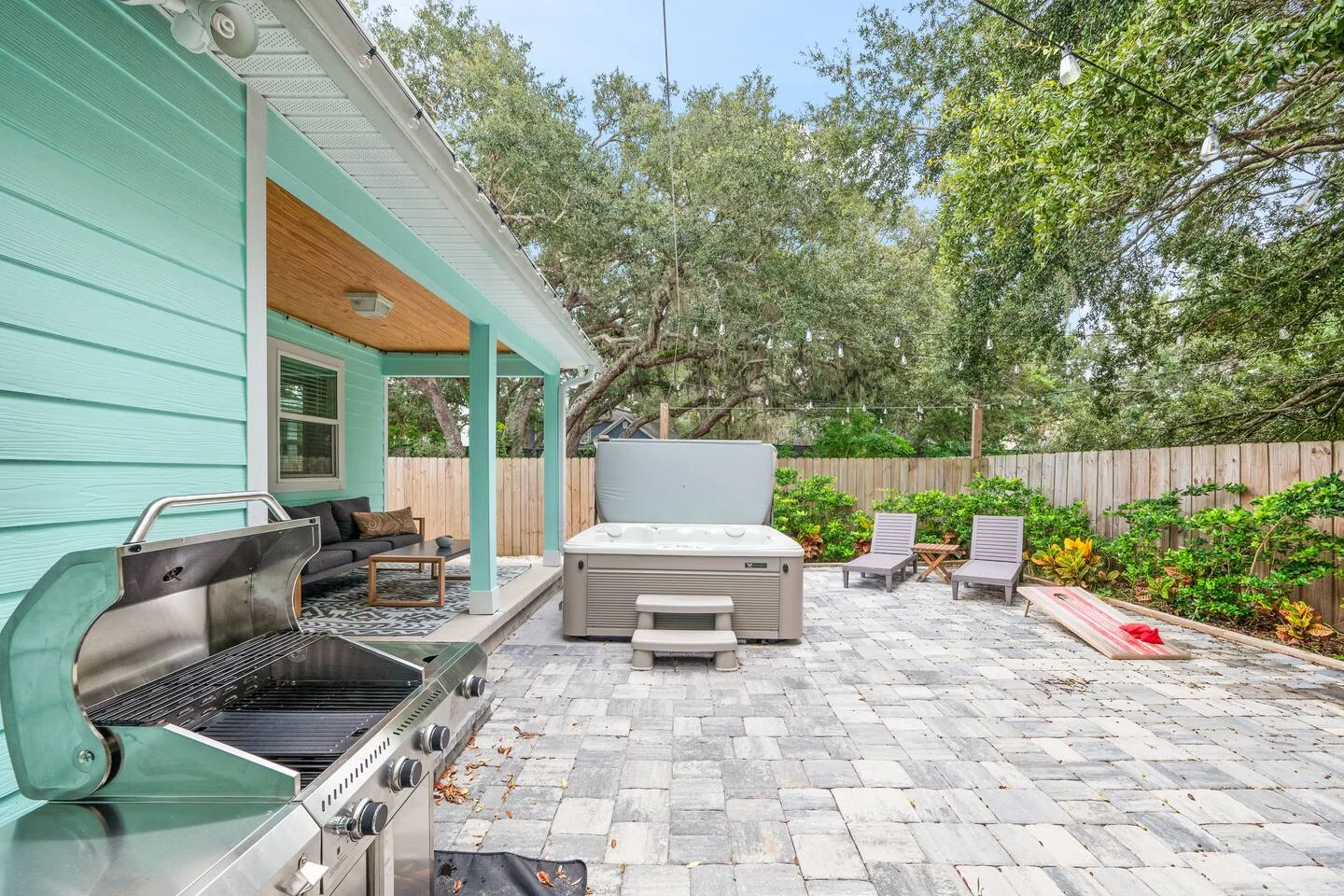 Luxurious backyard patio with turquoise house, hot tub, and gas grill surrounded by oak trees at The Yellow Butterfly