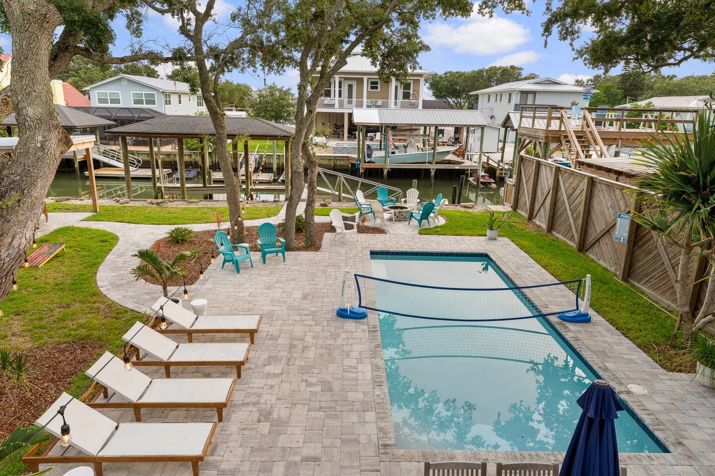 Waterfront pool with turquoise Adirondack chairs and boat dock overlooking calm water, showing why property managers choose
