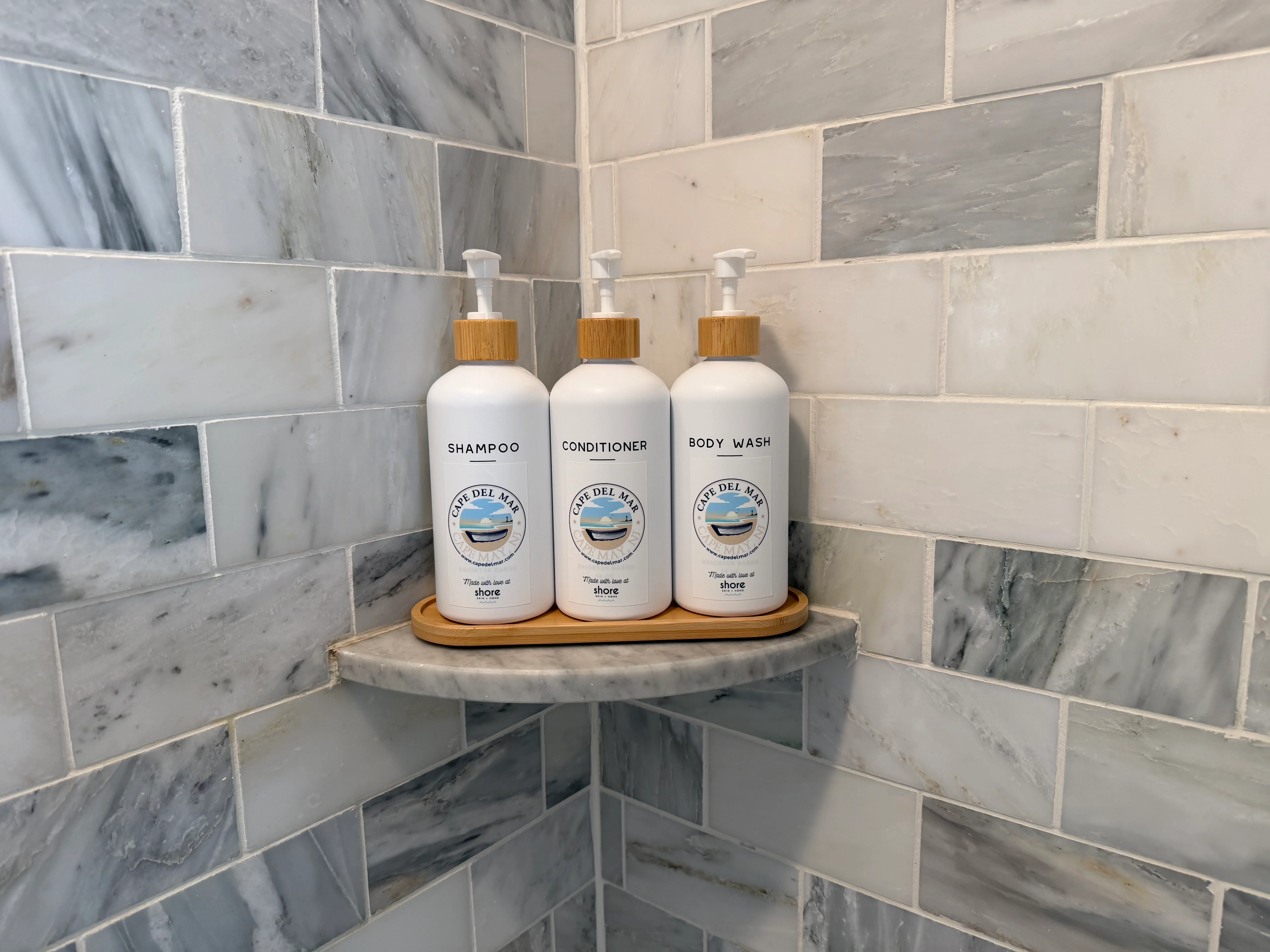 Luxury bathroom amenities at Cape Oar featuring coastal-themed shampoo, conditioner, and body wash bottles with marble tile