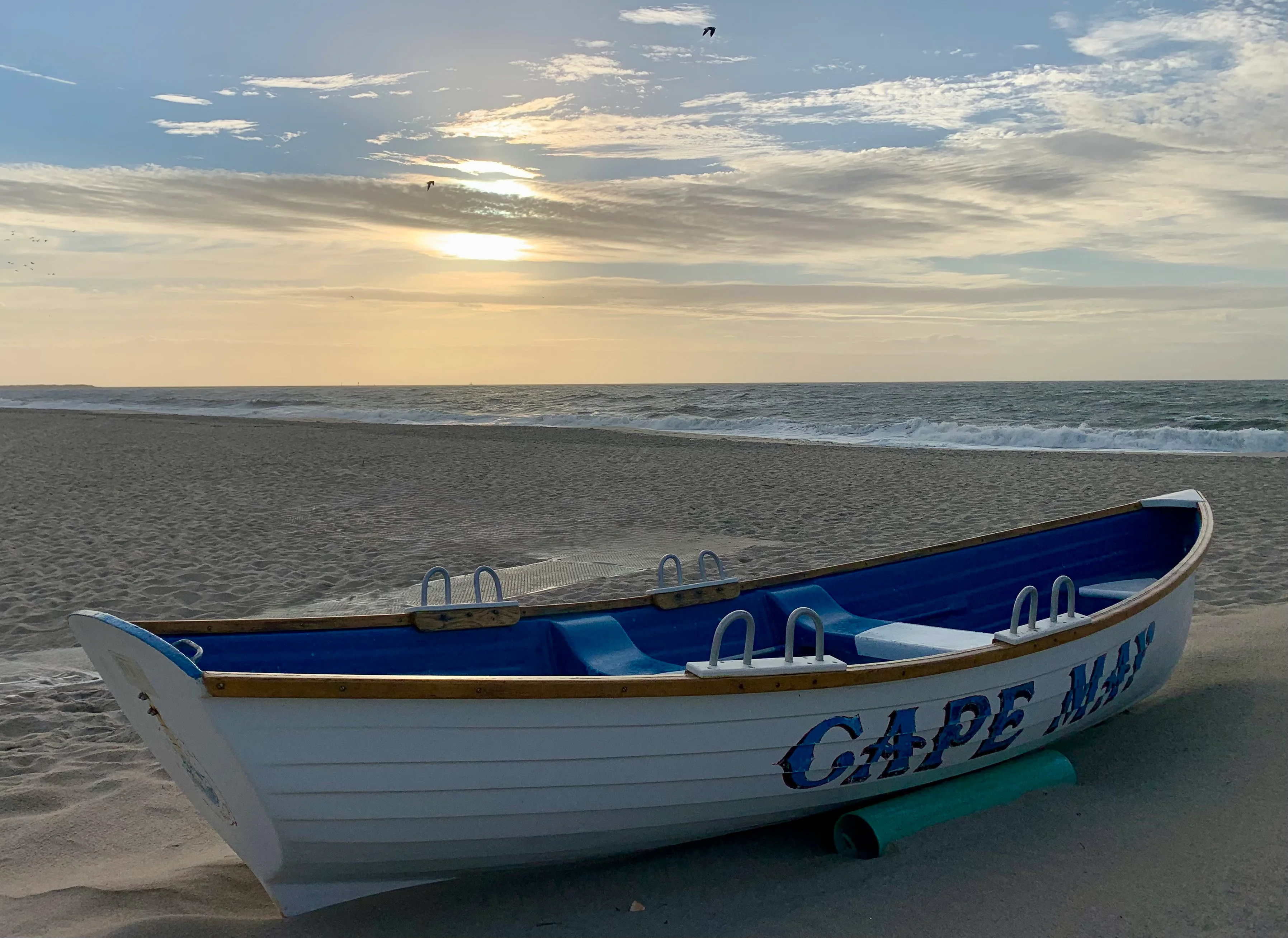 White and blue Cape May fishing boat on golden sand beach with ocean waves and coastal sky near Red Trail boardwalk