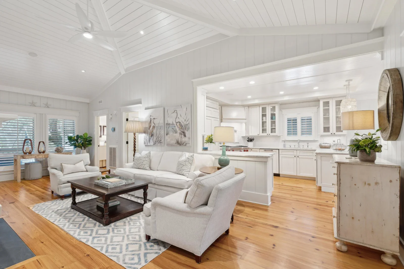 Bright coastal living room with white kitchen, cream furniture, and hardwood floors in a Kiawah Island vacation rental