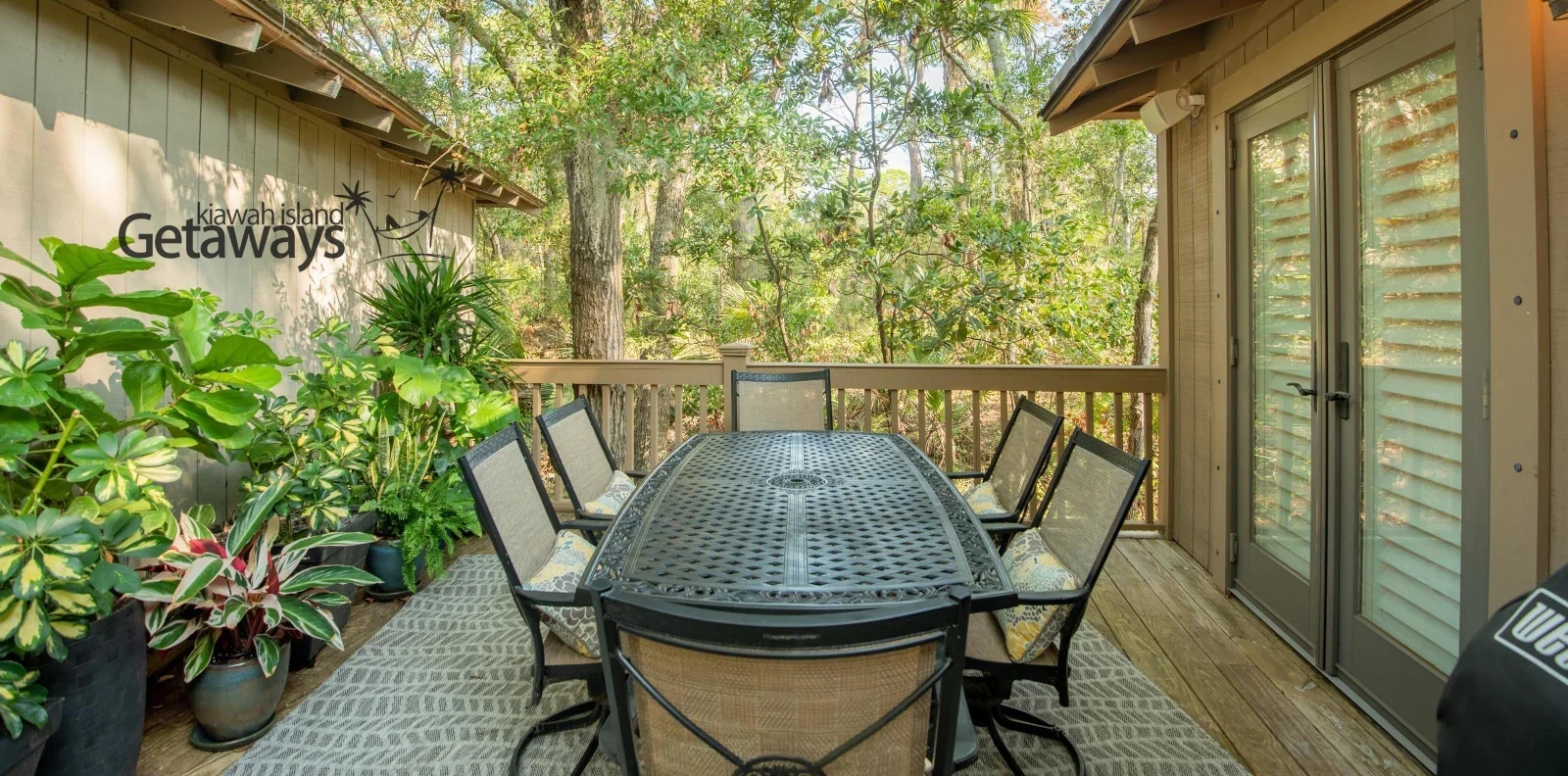 Outdoor patio deck with black dining table and lounge seating surrounded by potted plants and wooded privacy at Kiawah