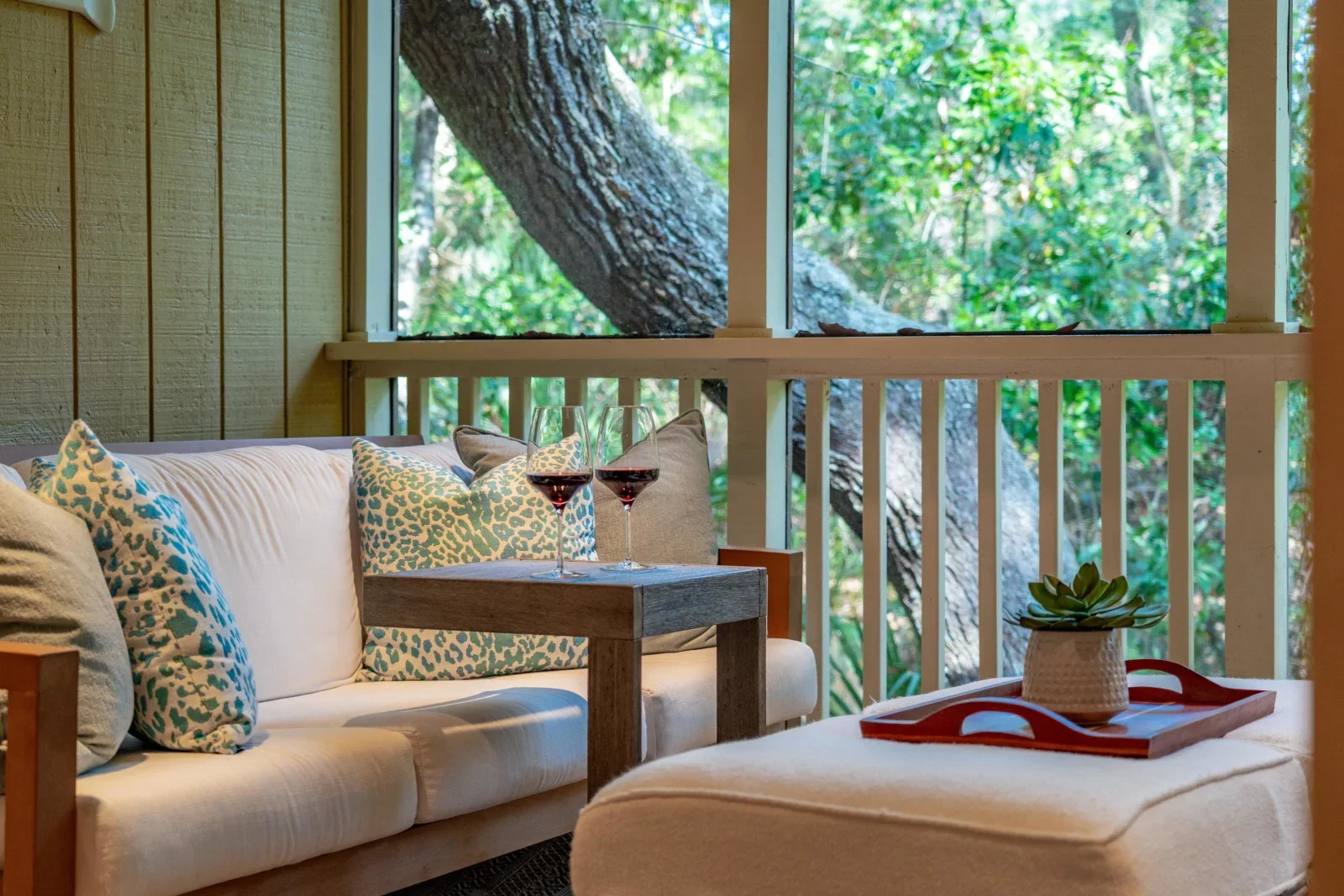Screened patio with cream sofa and wine glasses overlooking trees near Kiawah Island