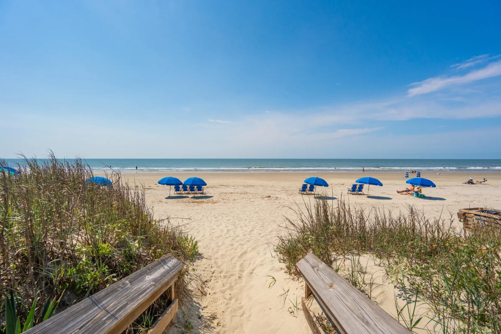 Sandy beach with blue umbrellas, chairs, and wooden walkways at Kiawah Island resort