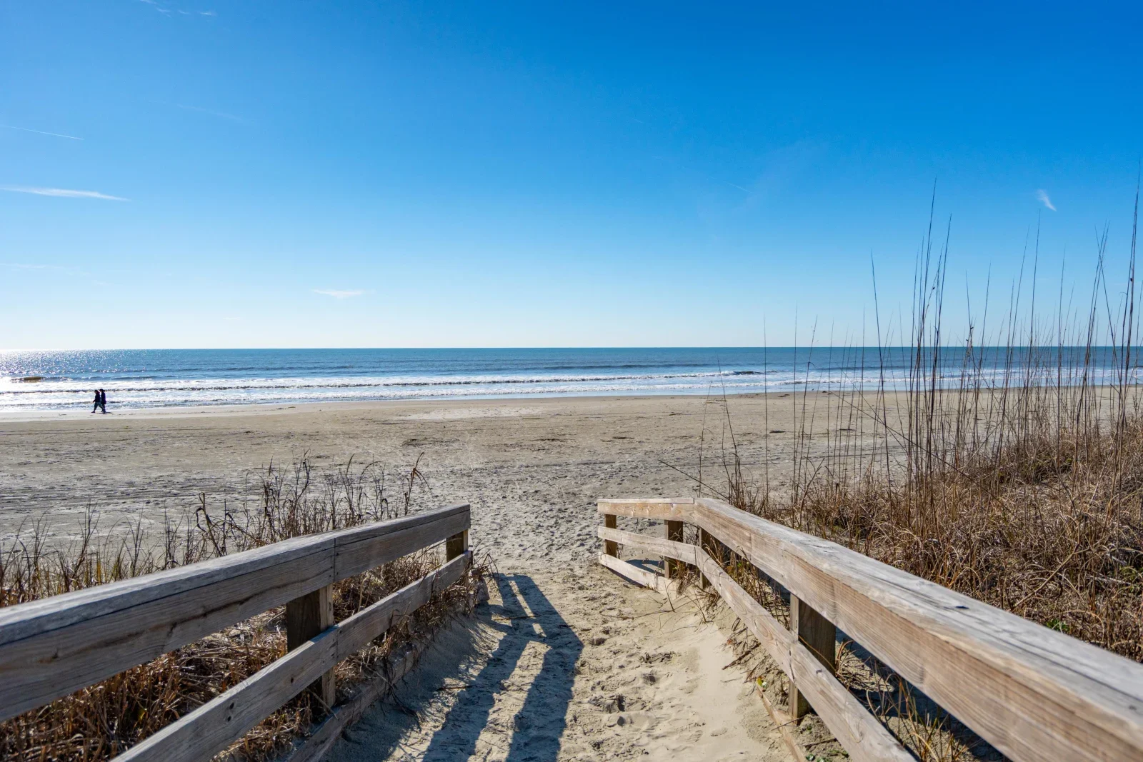 Wooden boardwalk with railings leading to sandy beach and dunes at Kiawah Island oceanfront home