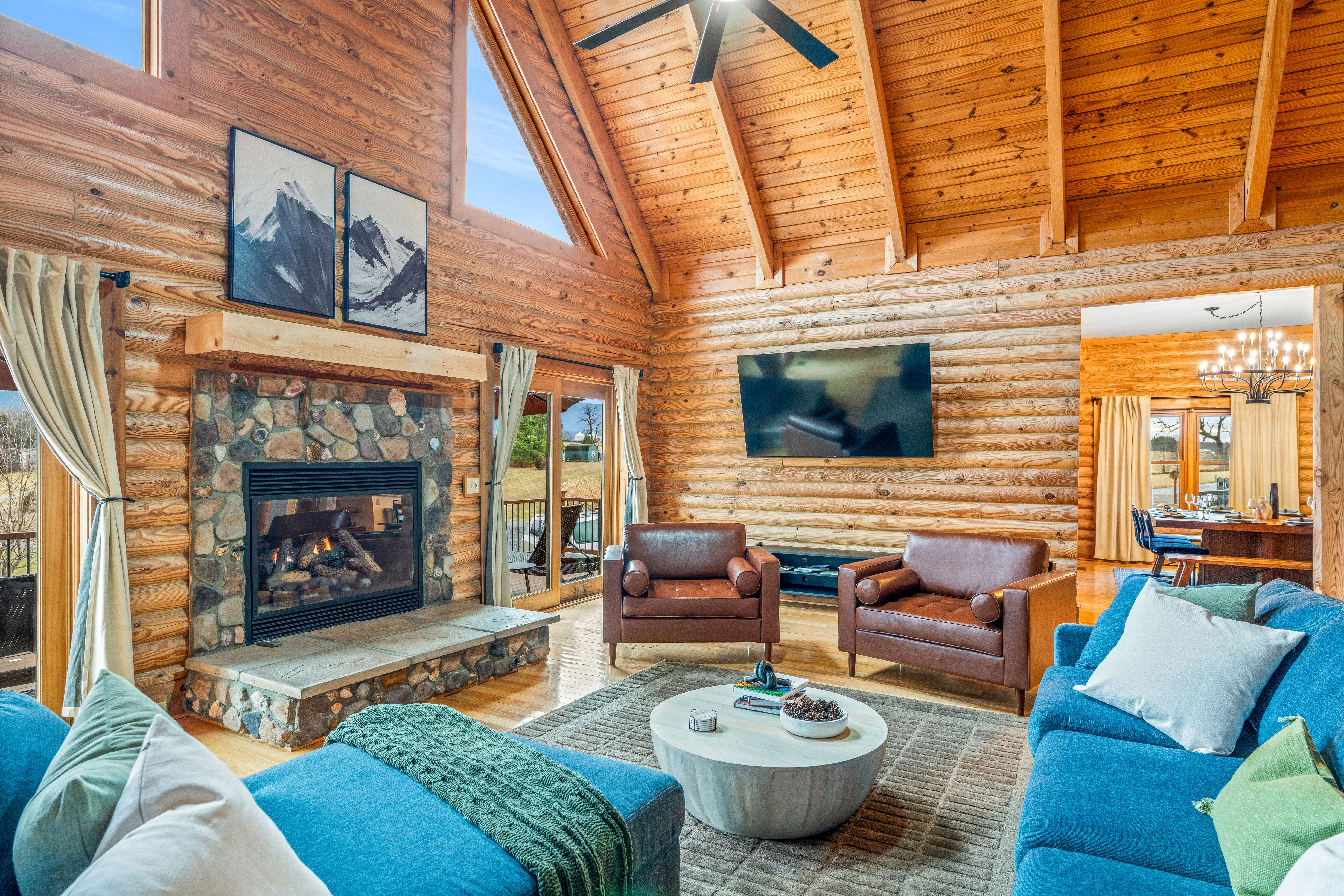 Log cabin living room with vaulted wood ceiling, stone fireplace, leather and blue seating in a Luray VA short-term rental