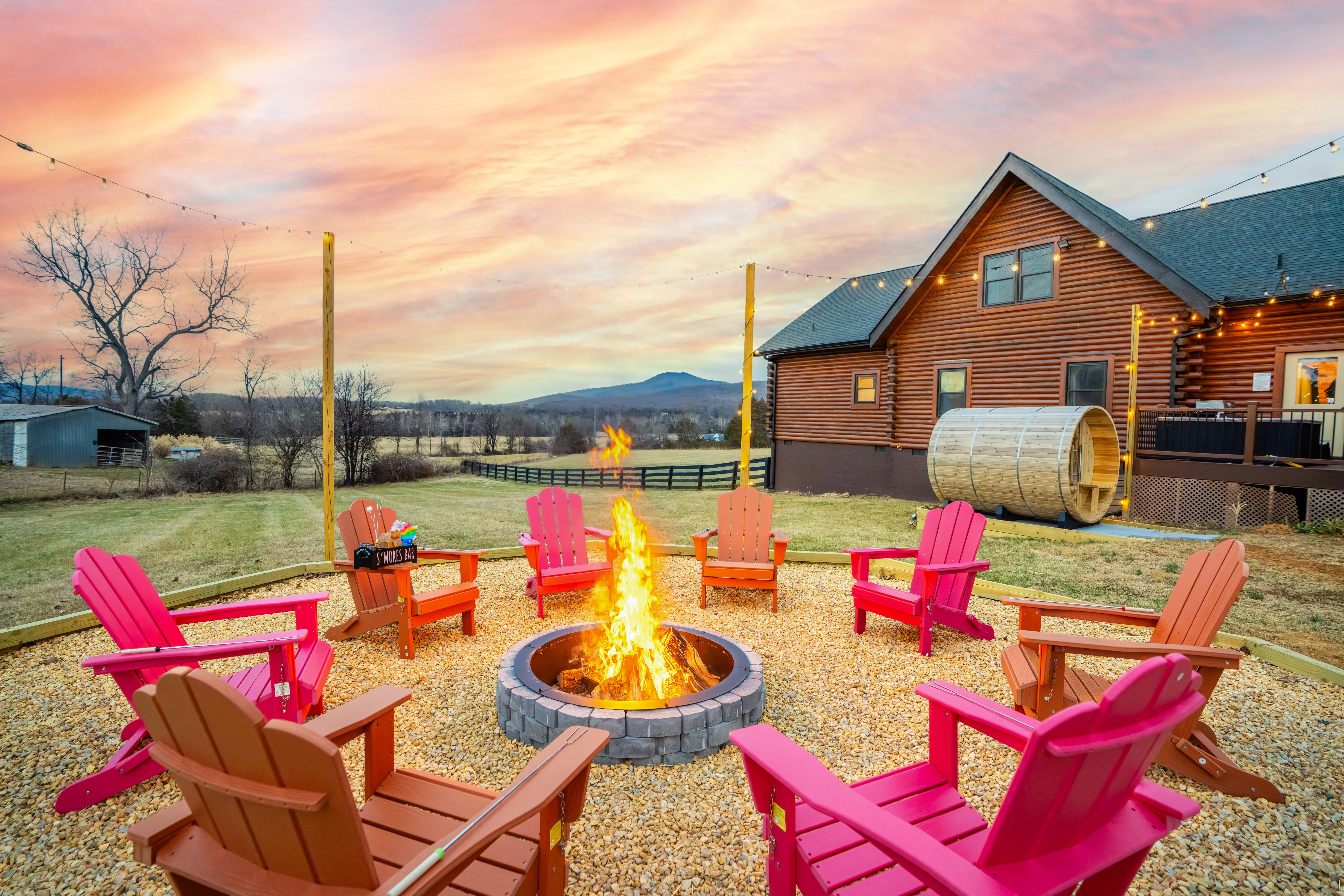Pink and orange Adirondack chairs around a fire pit at sunset, log cabin and mountain views in a Luray VA cabin for fall