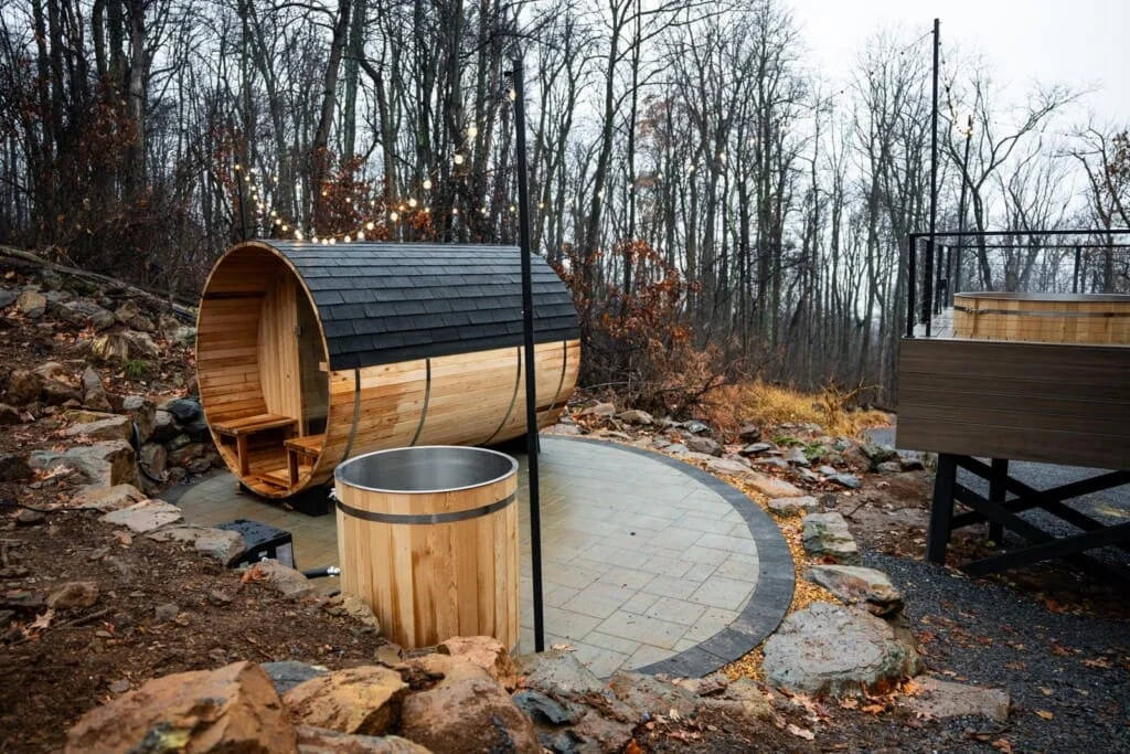Barrel sauna and wooden soaking tub with string lights in forest wellness cabin amenities near Shenandoah Valley