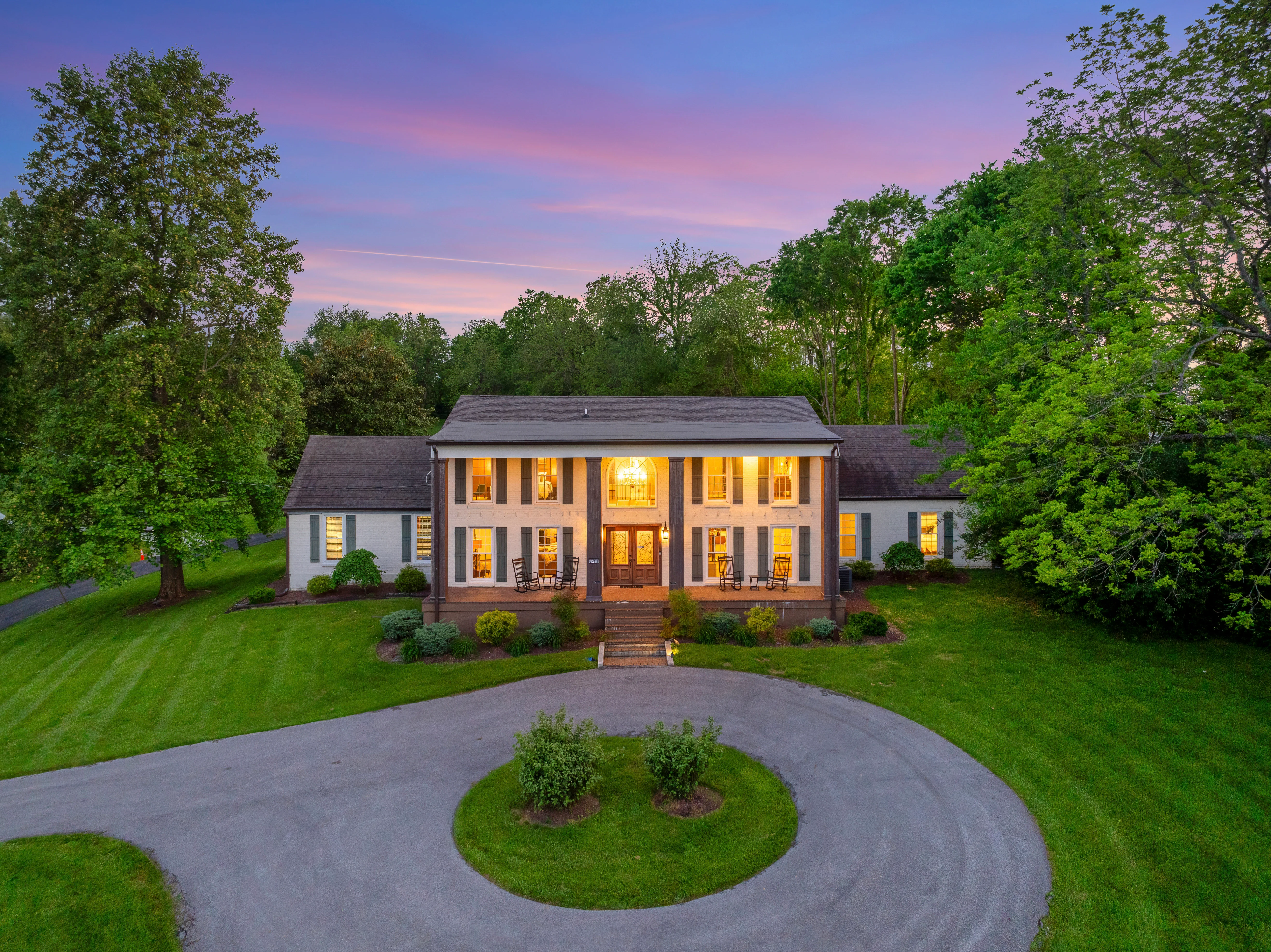 Colonial estate exterior with illuminated windows and circular brick driveway at Glencairn Knoll in Louisville